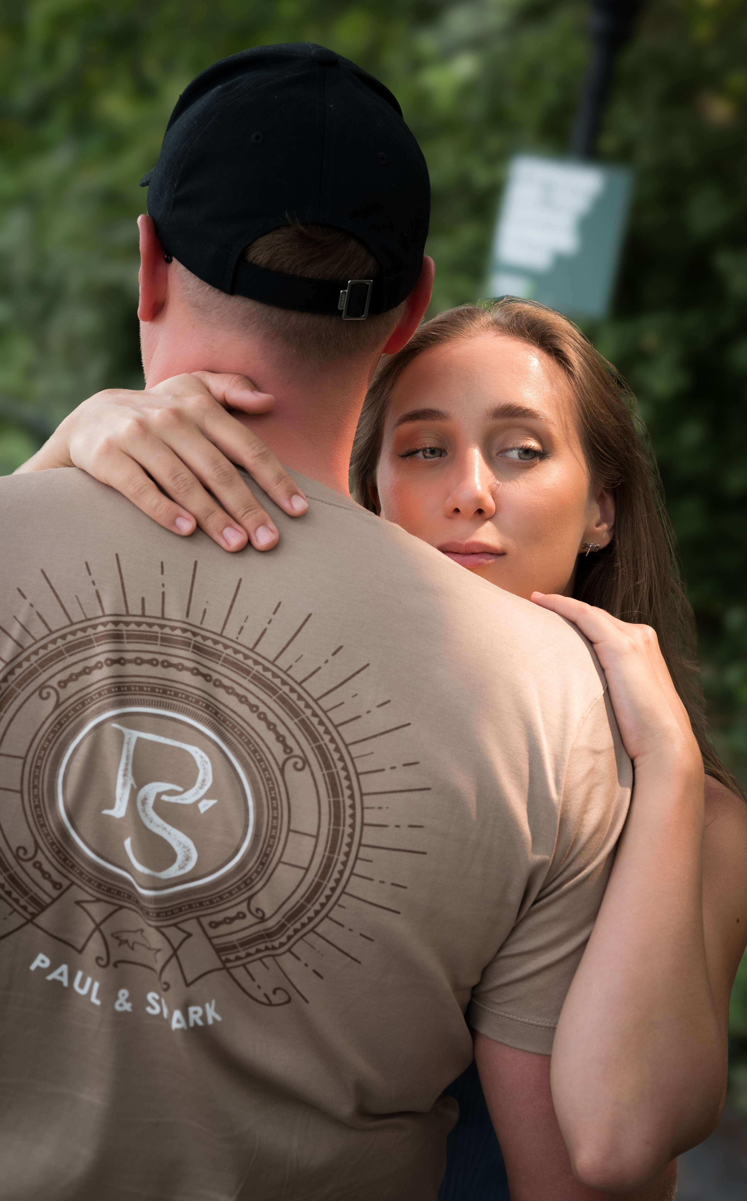 Close-up couple hug in a park, woman looking at camera while holding partner, natural light couple portrait.