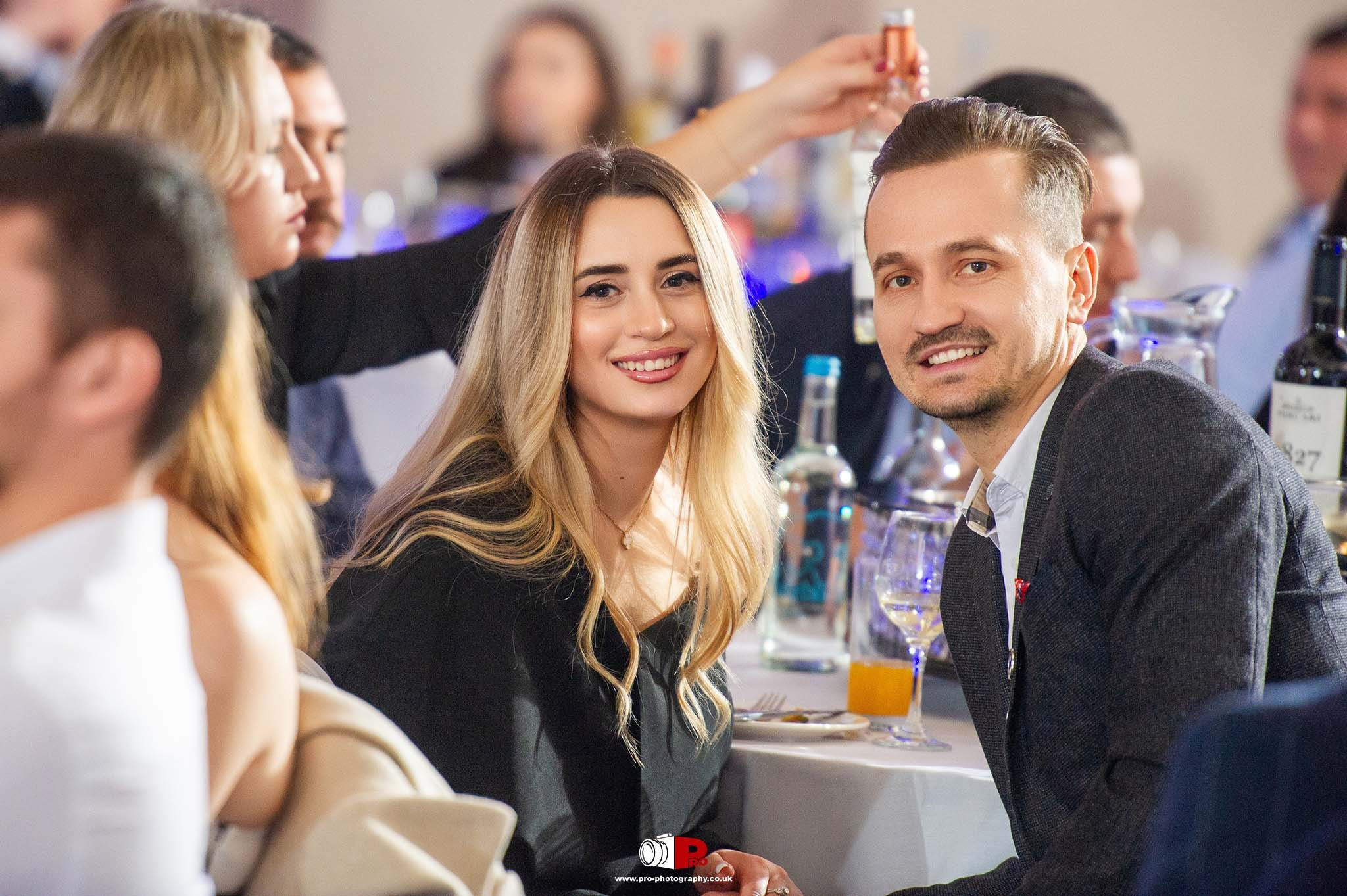 A  well-dressed, smiling couple of attendees are sitting in the front row, attentively watching the event unfold at the gala.