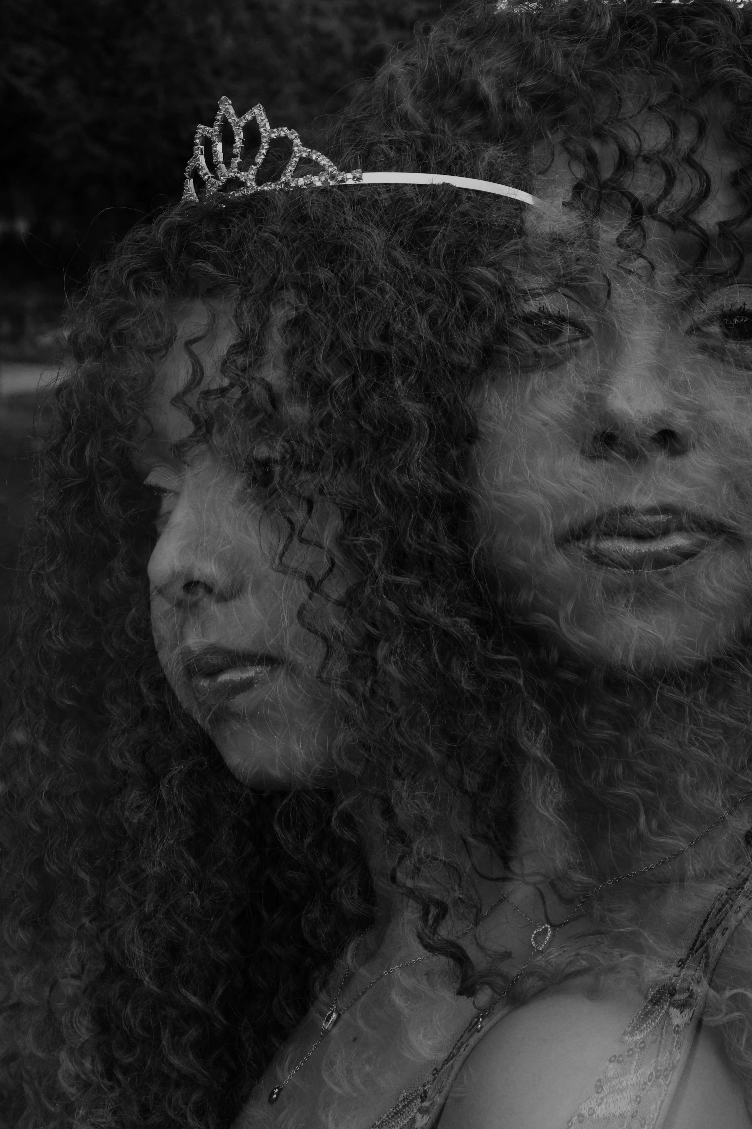 Fotografia em preto e branco com efeito de dupla exposição ou reflexo, mostrando o rosto de uma jovem com cabelos cacheados e uma tiara, com textura granulada estilo filme analógico