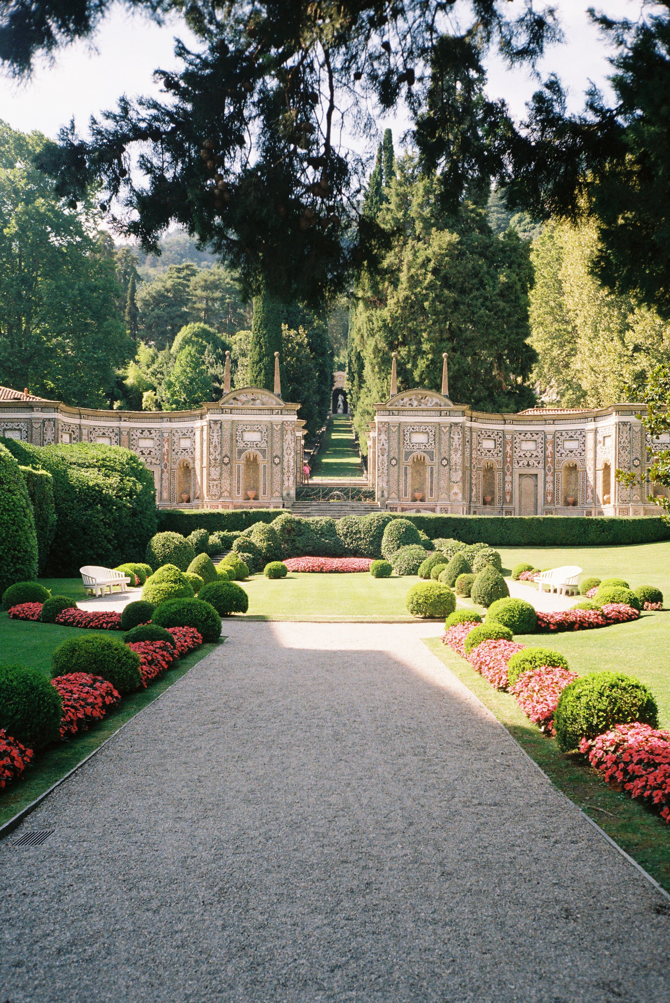 Lush Italian garden with symmetrical hedges, vibrant flower beds, and intricate stone wall backdrop.