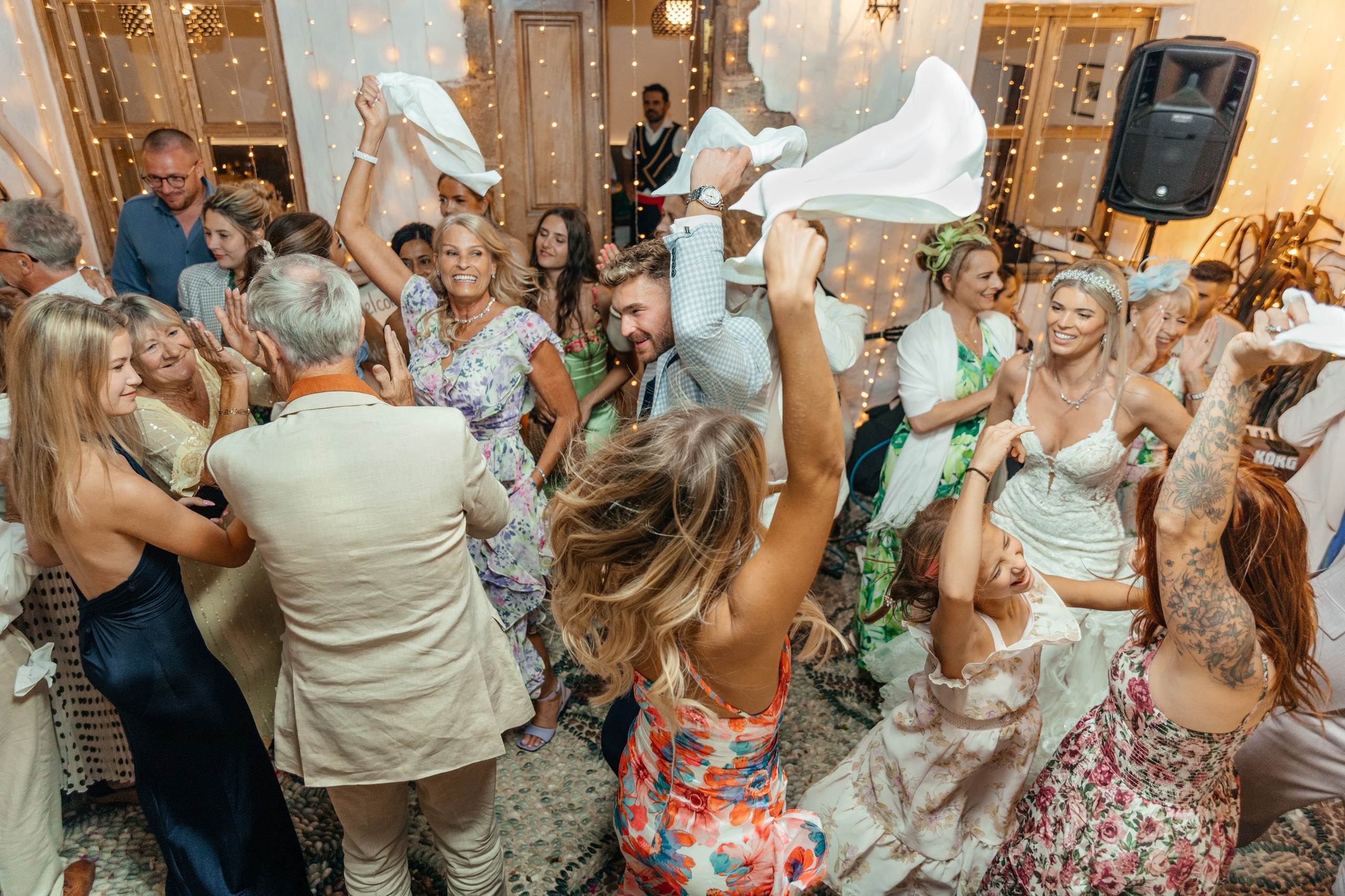Group of guests dancing and celebrating at the wedding party in a traditional Greek restaurant in Lindos, with the couple joining in the fun.