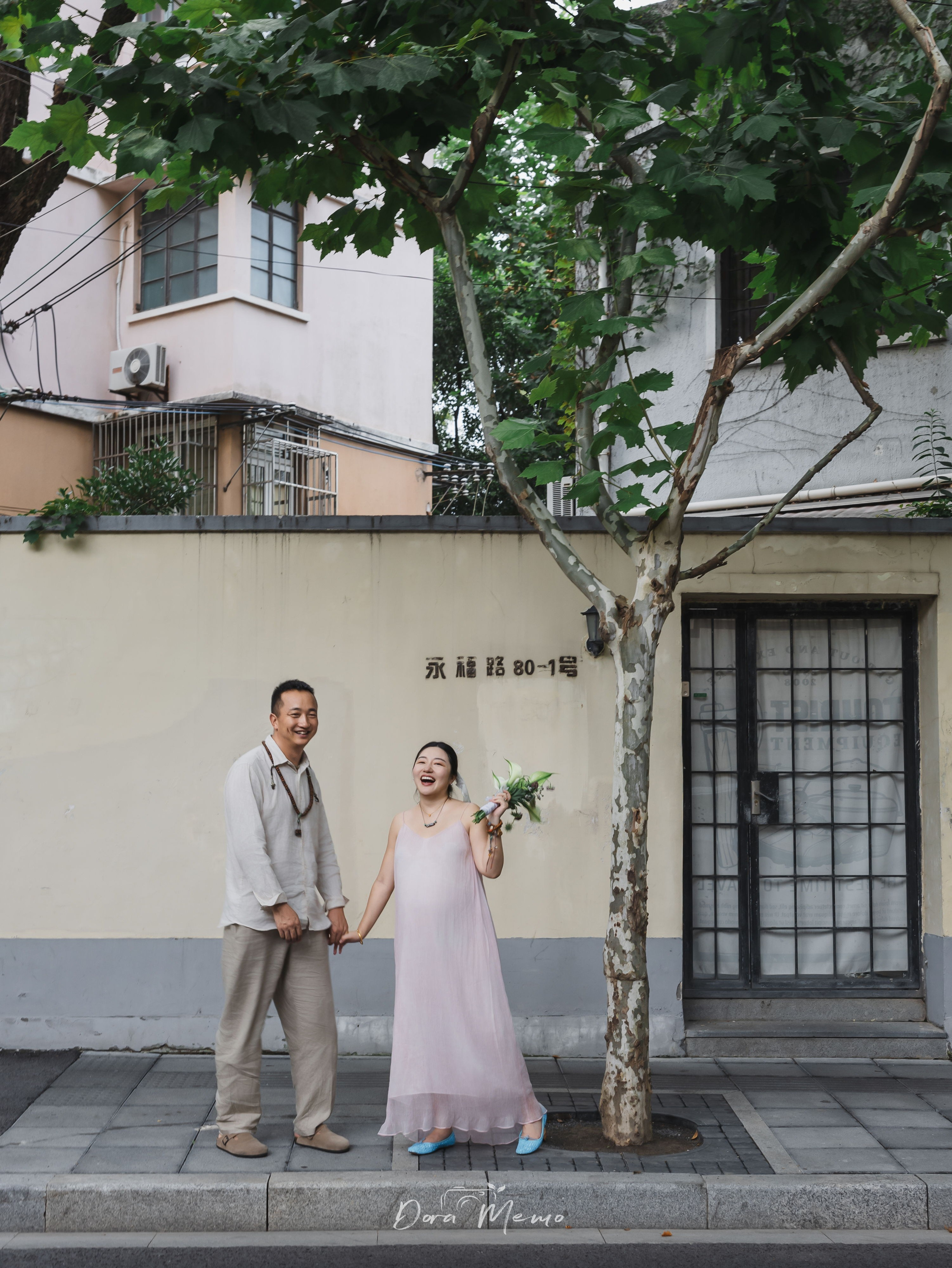 Pregnant woman laughing while holding hands with her partner on a city sidewalk, photographed by a Shanghai family photographer capturing everyday life.