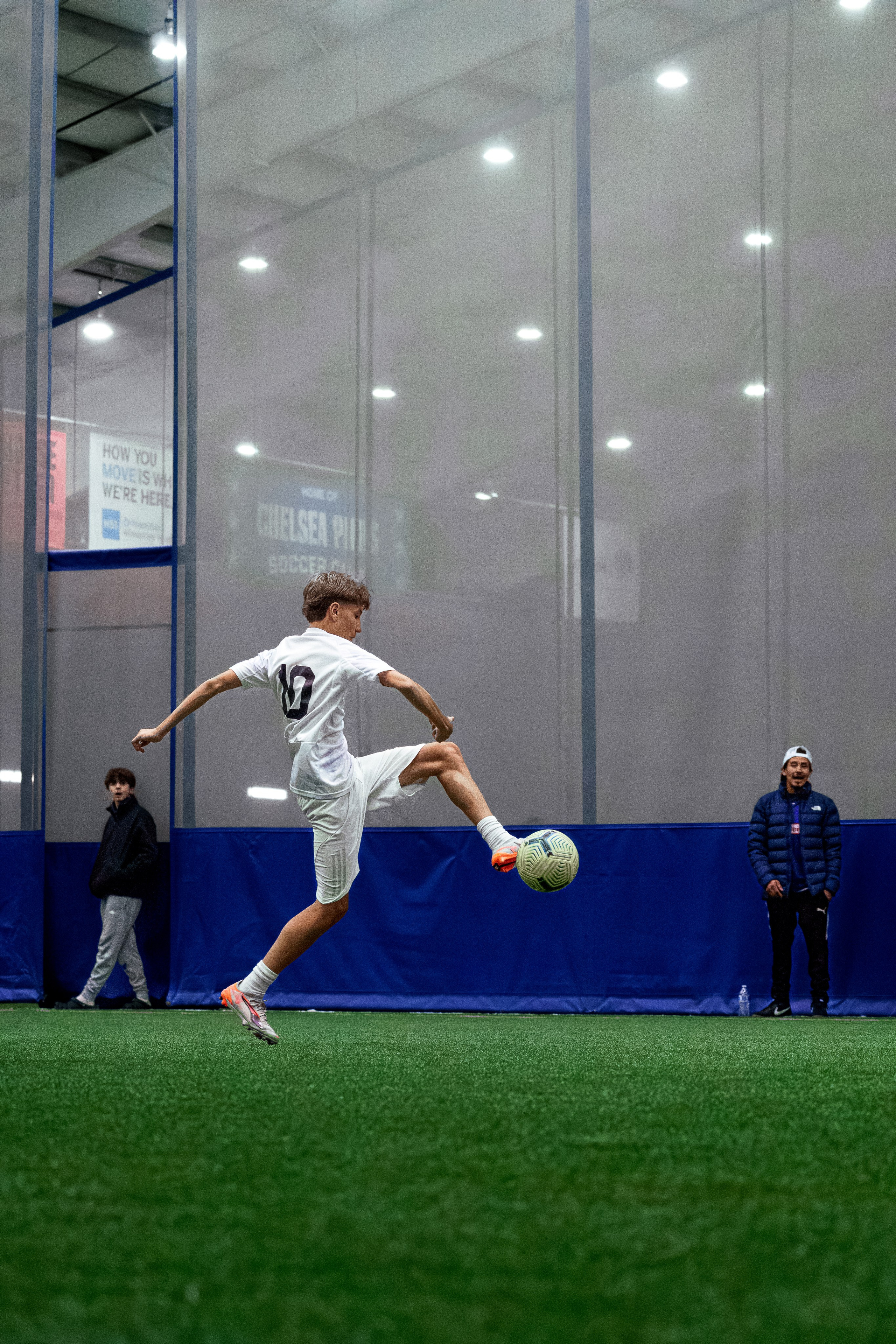 Indoor soccer player striking the ball on turf inside a bright training facility. Trying to take a touch.