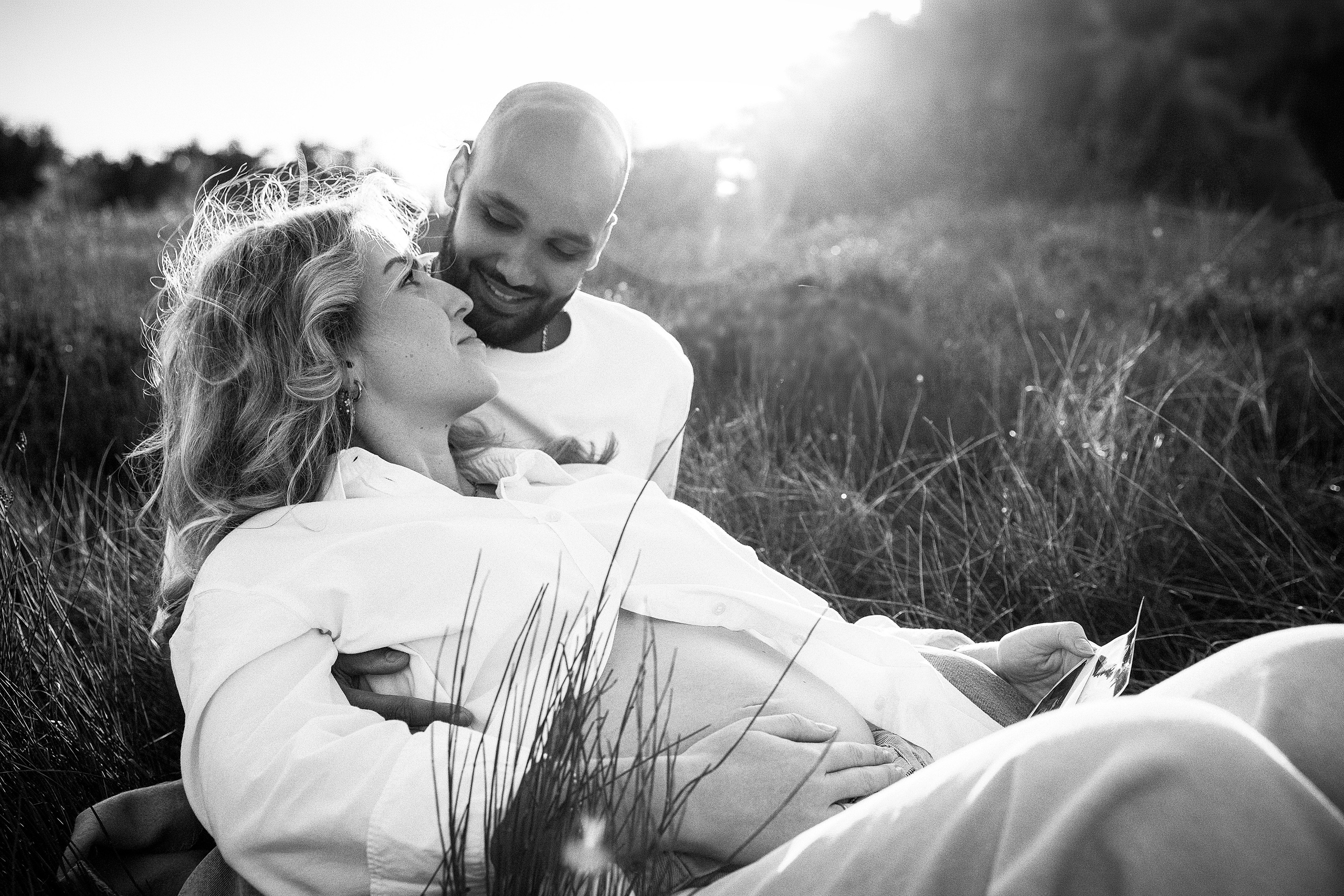 Sesión de fotos de embarazo en Valencia, España, con una pareja embarazada abrazándose en un entorno natural al aire libre, capturada con luz suave para un momento cálido y emotivo — ideal para fotografía de embarazo en Valencia y en toda España.