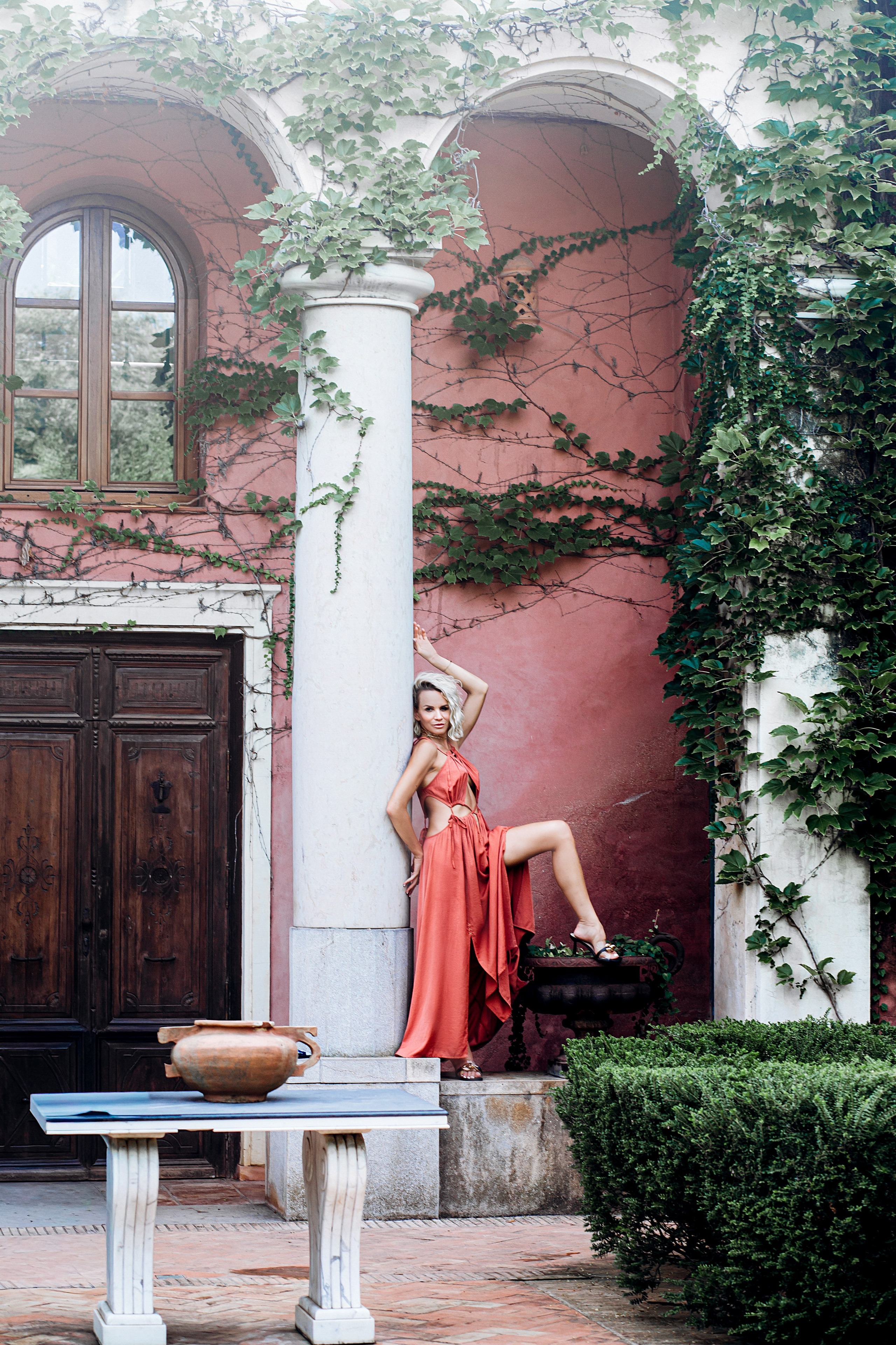 Элегантная портретная съёмка в Шативе, Испания — женщина в красном платье уверенно позирует под арками, увитыми плющом, на фоне средиземноморской архитектуры. Идеальное вдохновение для стильных фотосессий в Шативе и живописных испанских городах.