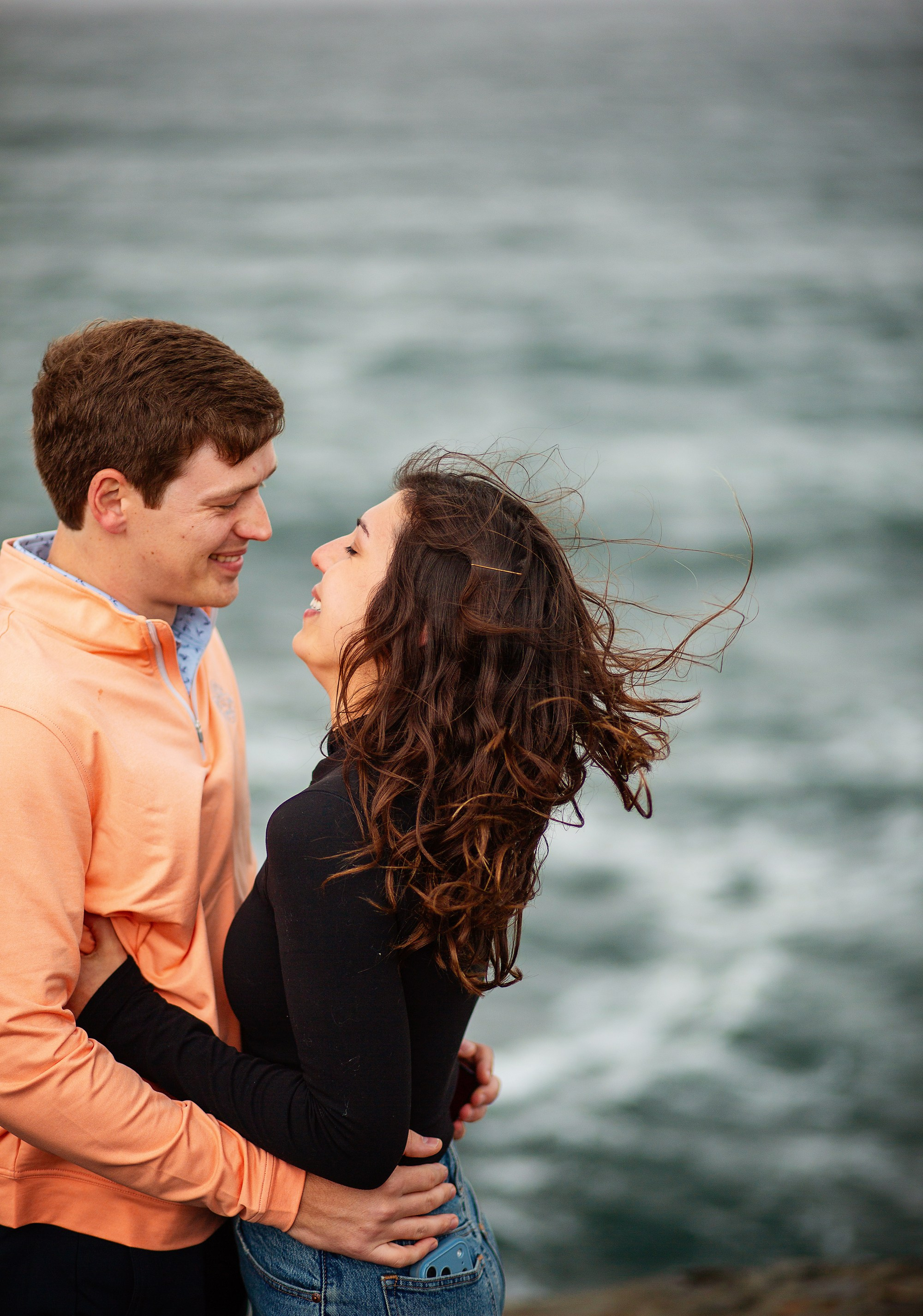 Newly engaged couple smiling at each other on the rugged cliffs of the Irish coast.