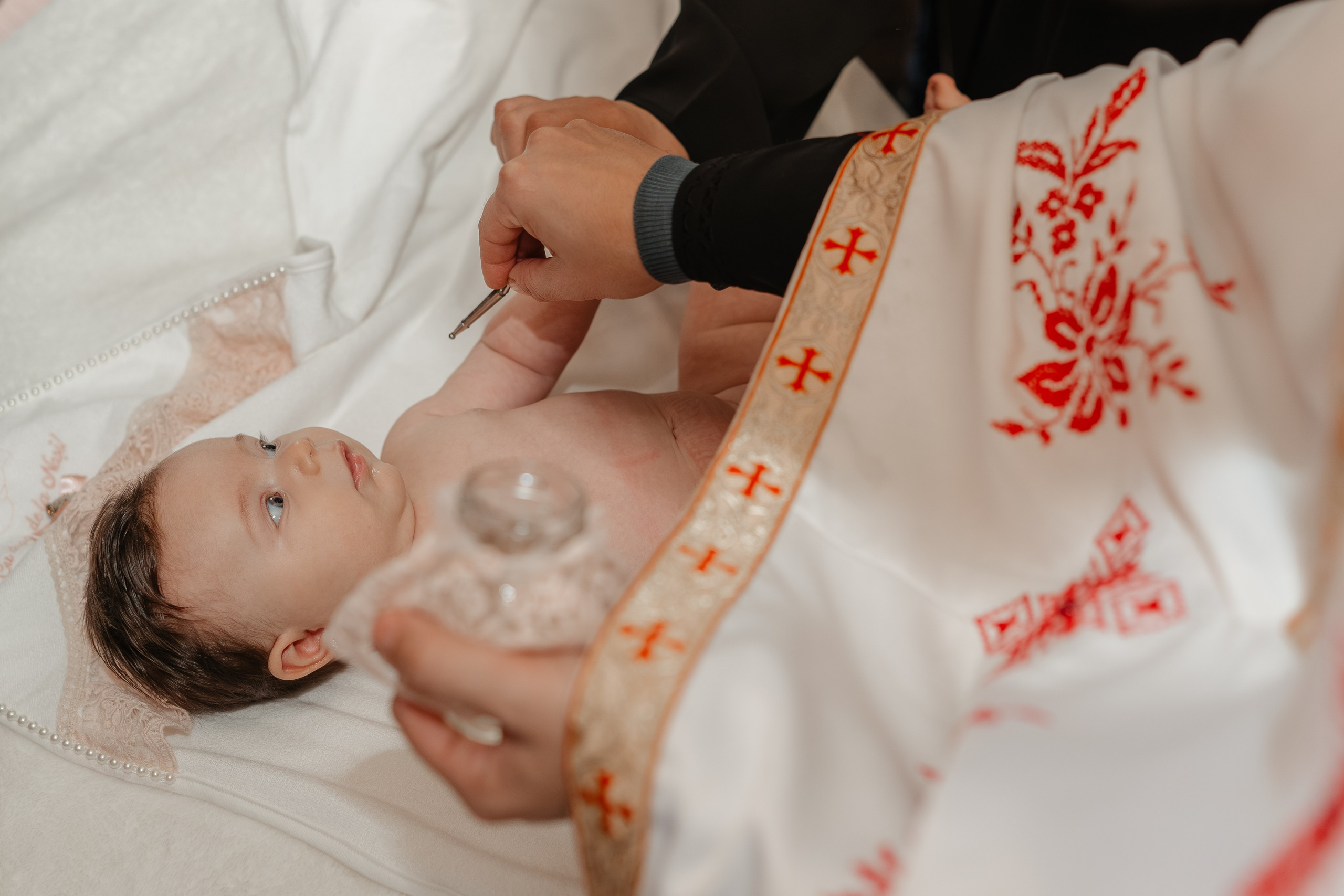 Ritualul ungerii cu mir sfânt la botezul Evelinei Maria. Preotul unge solemn pruncul așezat pe masa botezului, în timp ce nașii și familia asistă. Moment sacru și de profundă simbolistică.