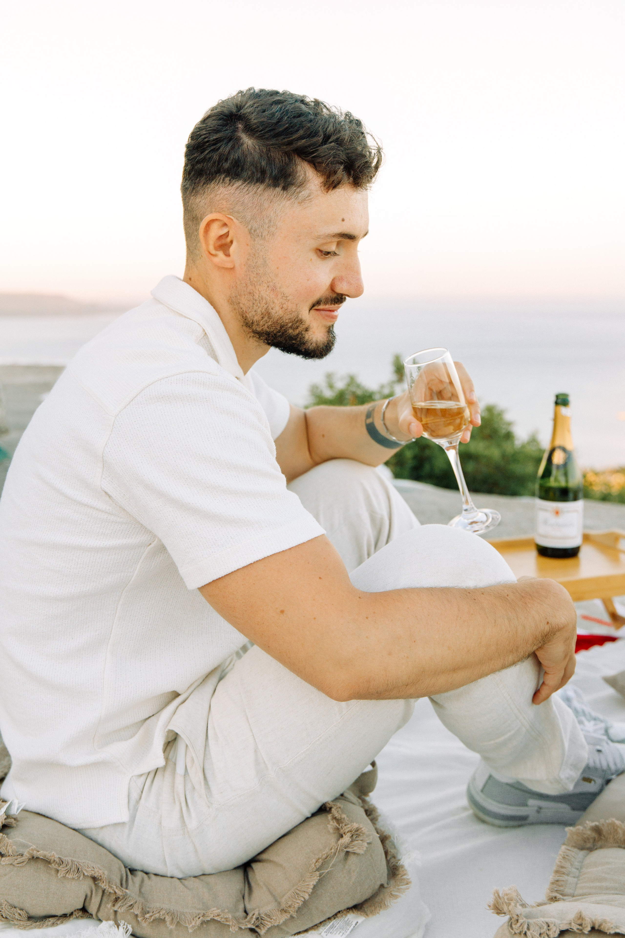 "Anstoßen auf die Liebe: Ein Paar genießt ein Glas Sekt nach dem Heiratsantrag auf dem Profitis Ilias, hoch über der Küste von Faliraki und dem azurblauen Mittelmeer."