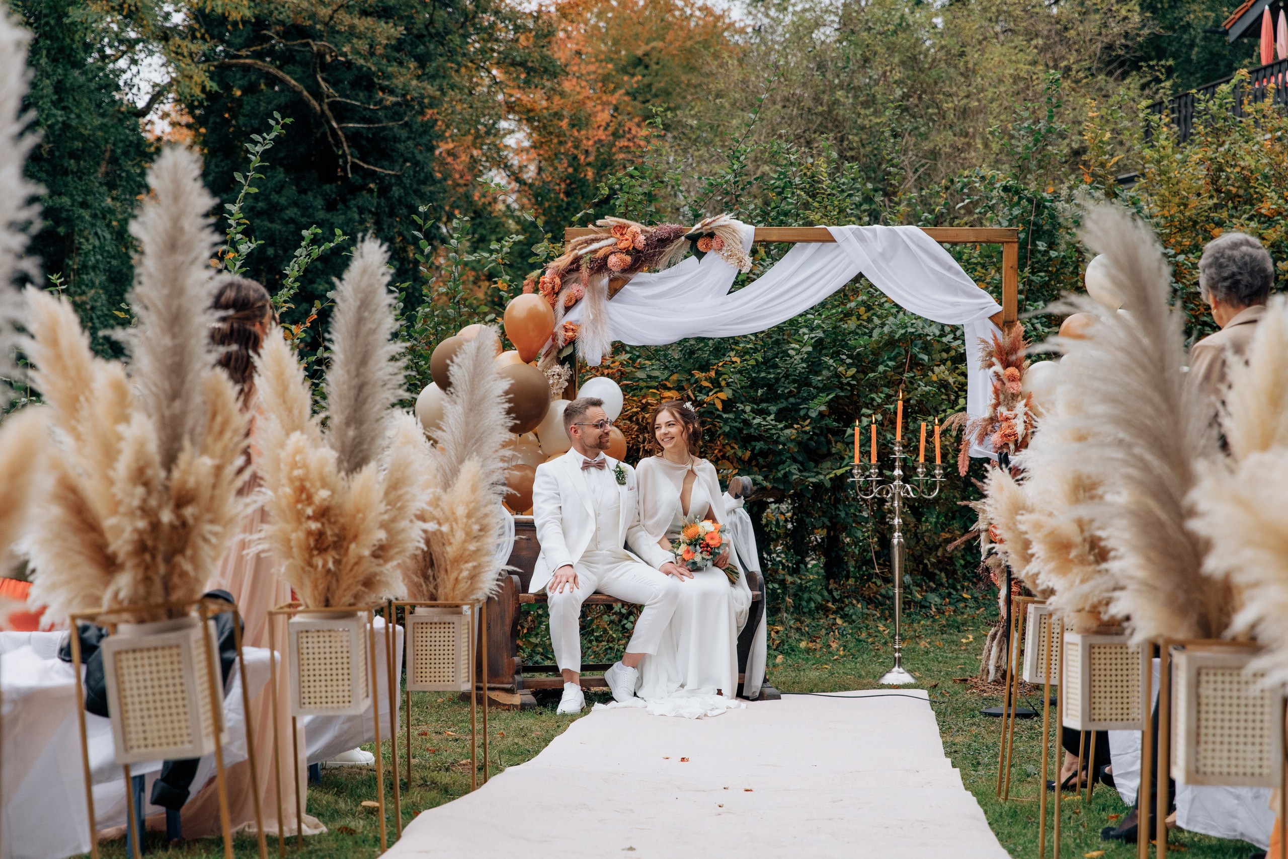 Der Bräutigam und die Braut sitzen auf einer antiken Bank unter einem Hochzeitsbogen, umgeben von Hochzeitsdekoration.