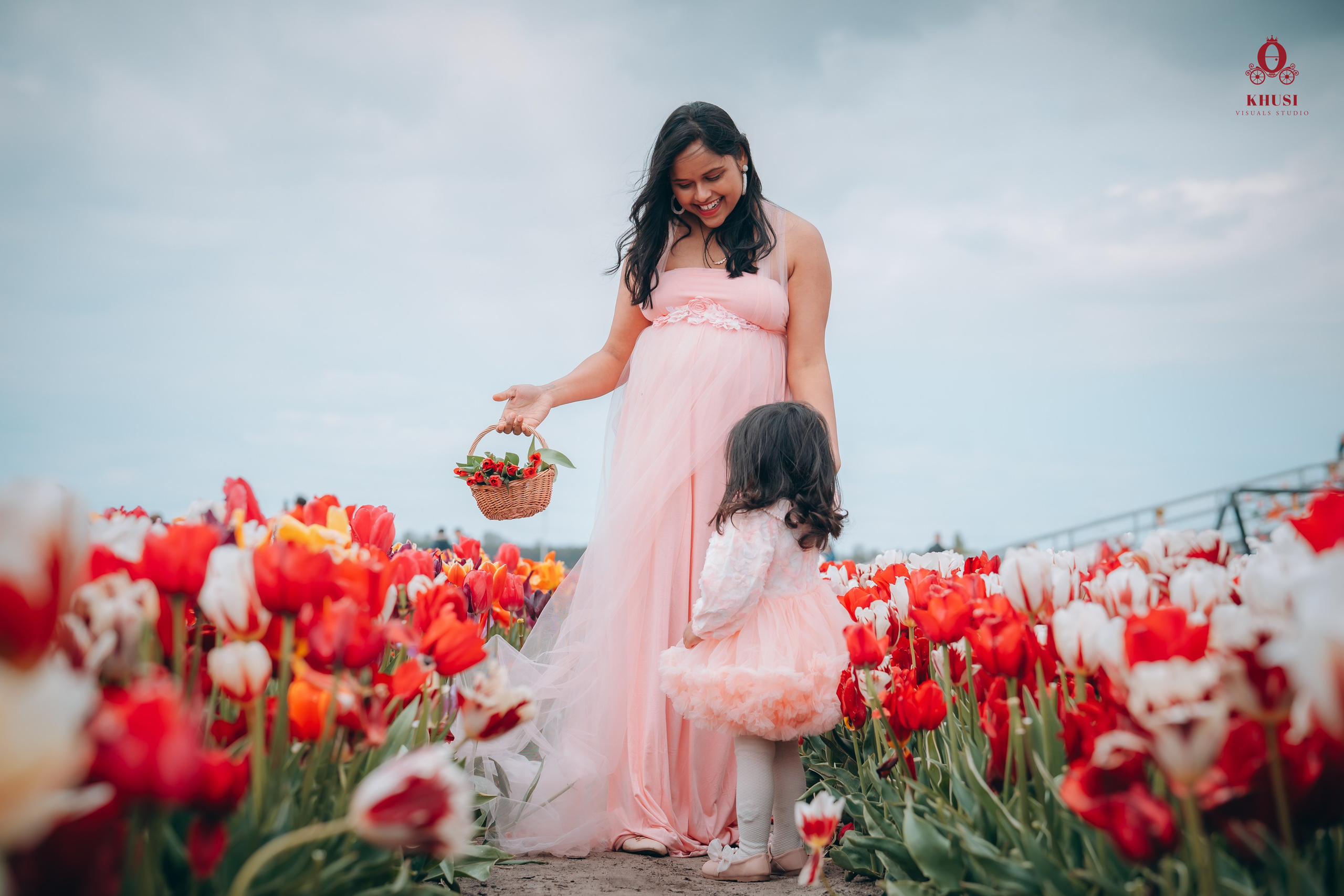 A girl kid running towards her pregnant mother holding tulips basket in tulip fields of Netherlands.