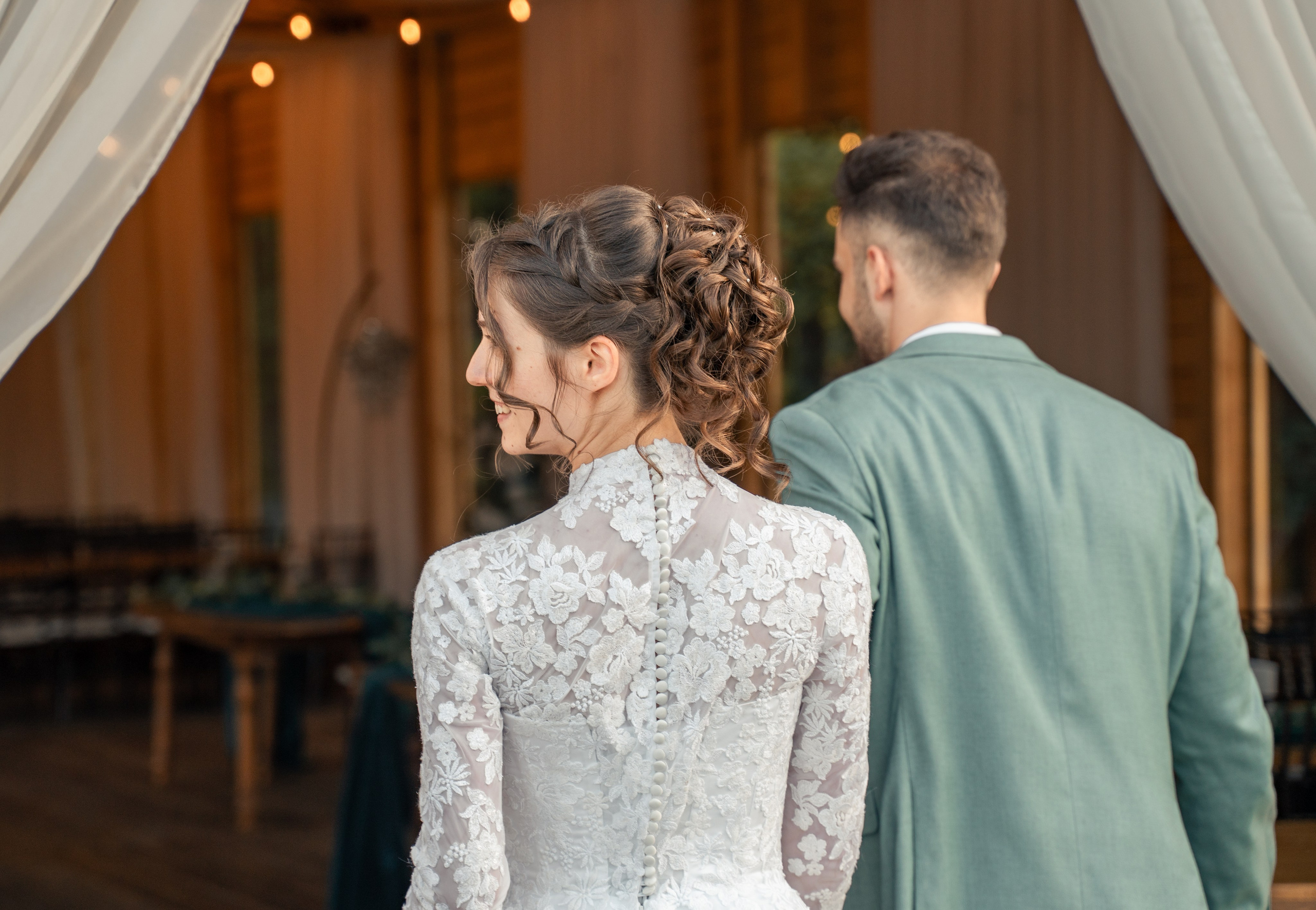 Vedere din spate cu mirii intrând la recepție, rochie de mireasă cu dantelă și nasturi, coafură elegantă, incadru.ro.