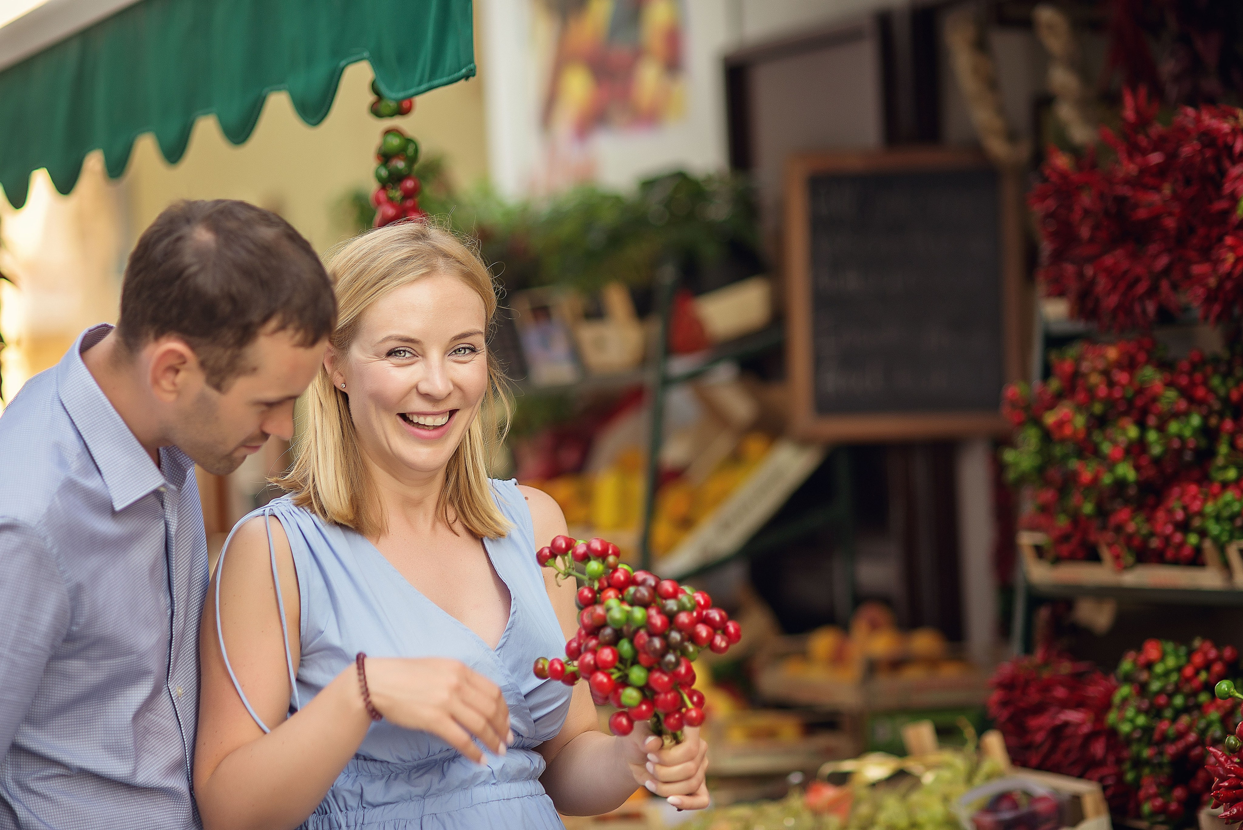 Woman smiling with a bunch of decorative chili peppers in hand, her partner beside her. A joyful and light moment.