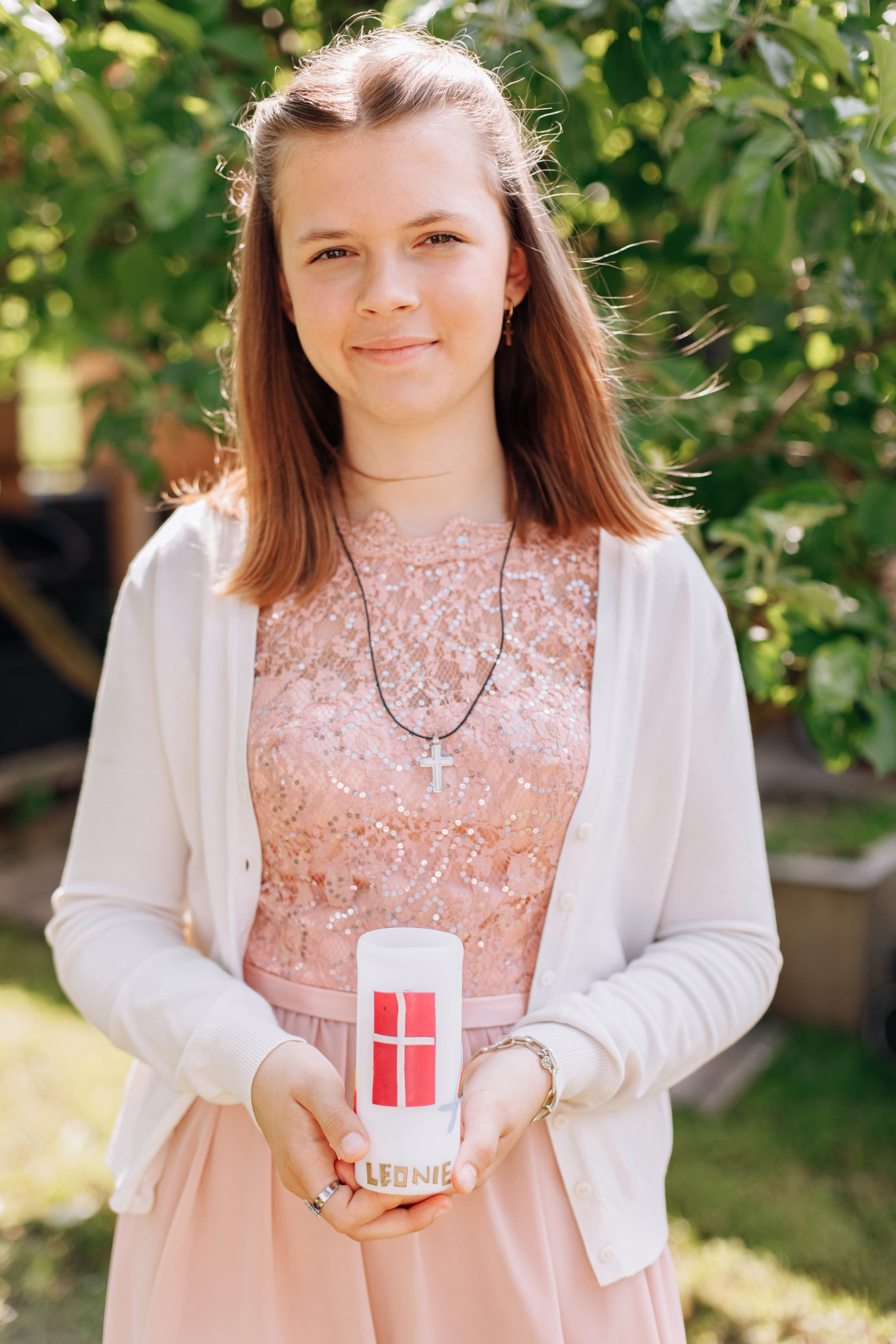 Mädchen steht im Sommergarten mit einer Konfirmationskerze.