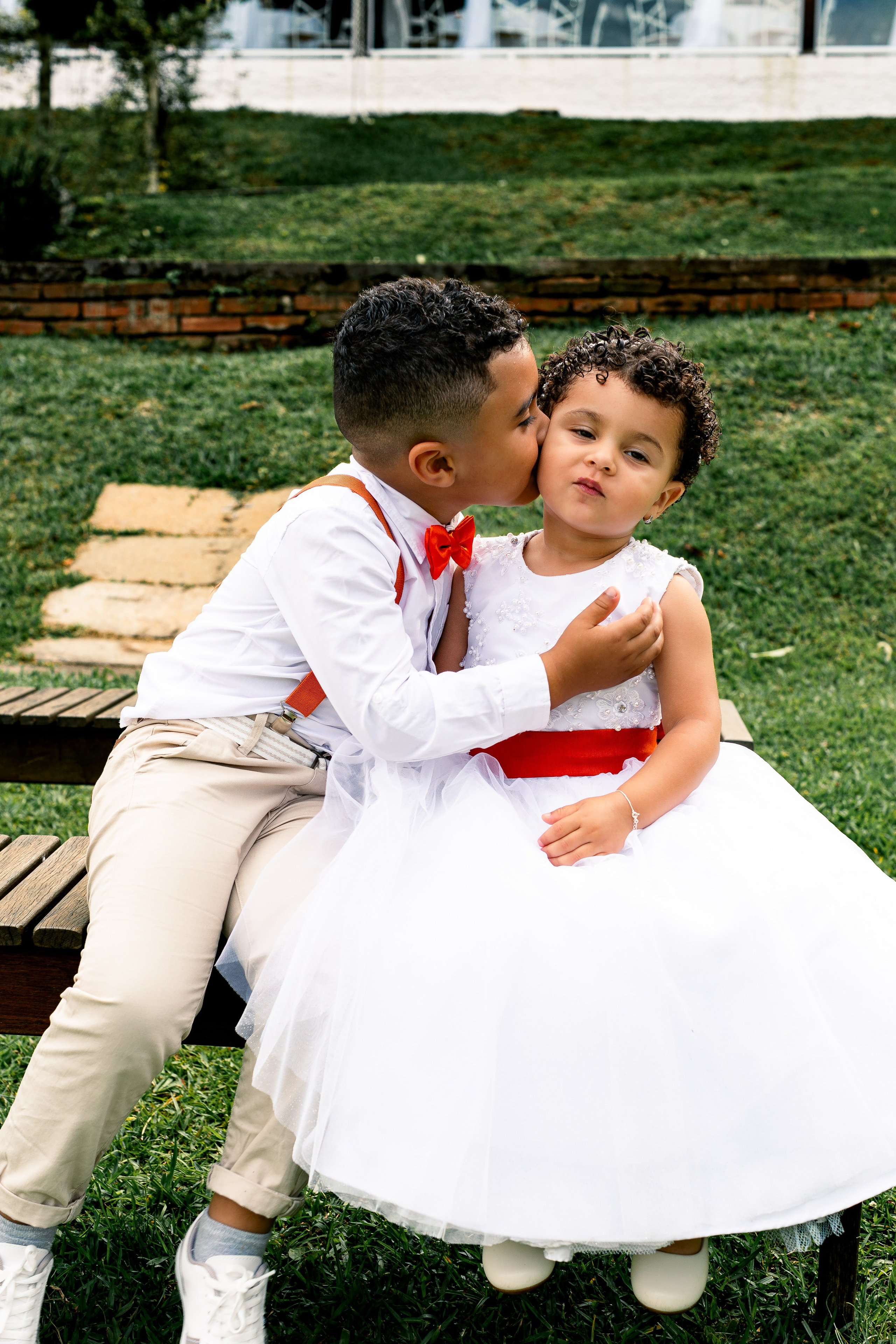 Pajem dando beijo carinhoso na irmã durante o casamento dos pais, momento doce e inesquecível.