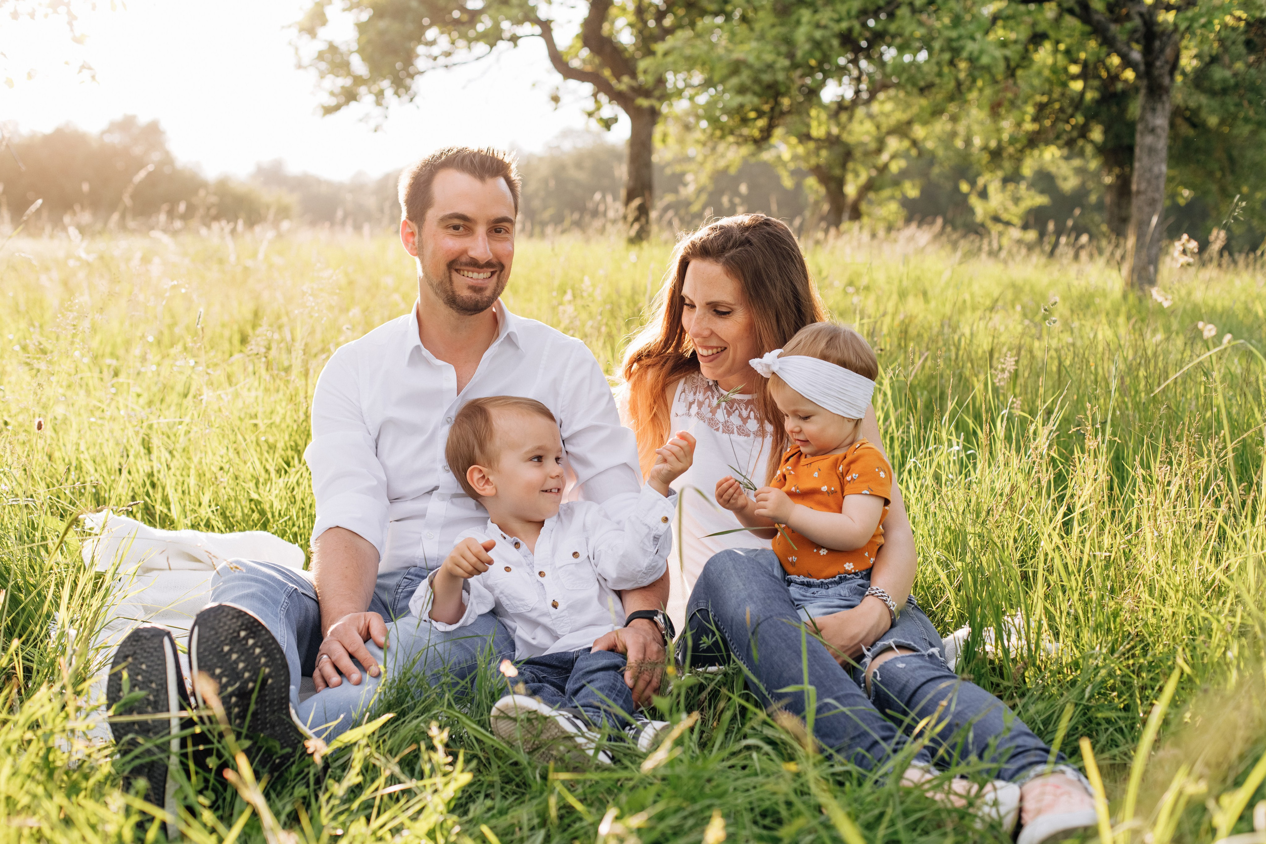 Die Familie sitzt auf einer grünen Wiese und lacht gemeinsam.