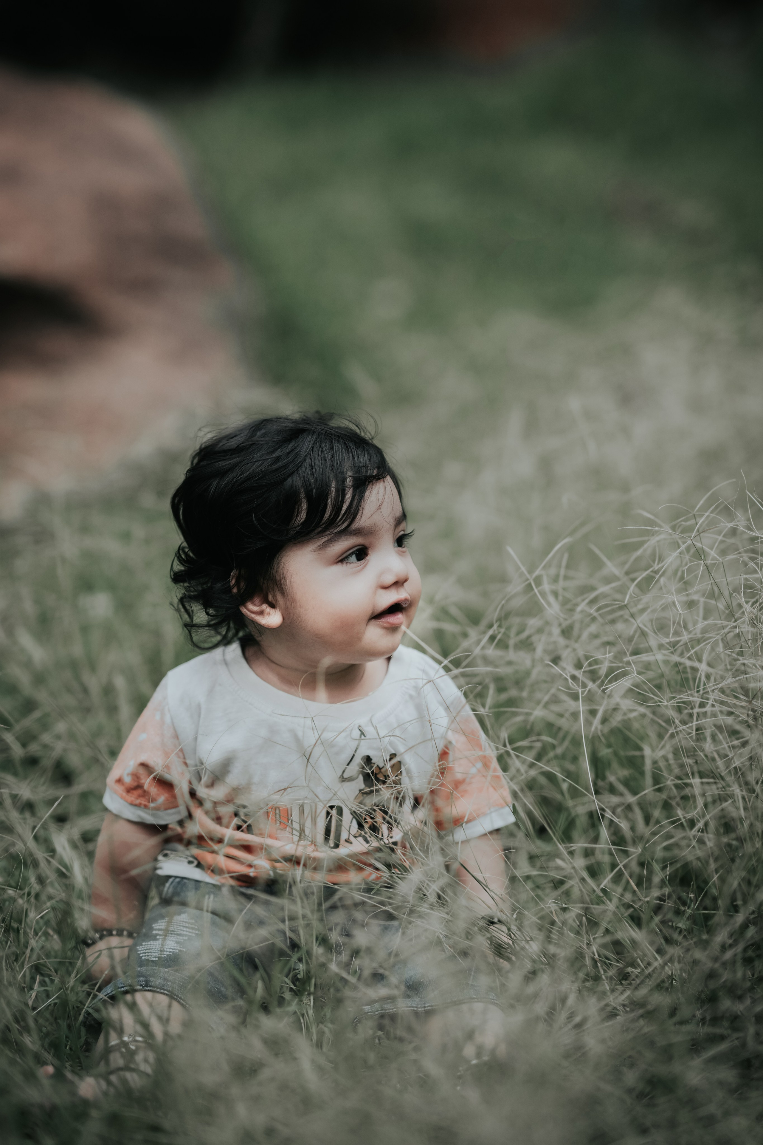 candid outdoor portrait of a young child with dark hair sitting in tall grass in Malleshwaram, Bengaluru