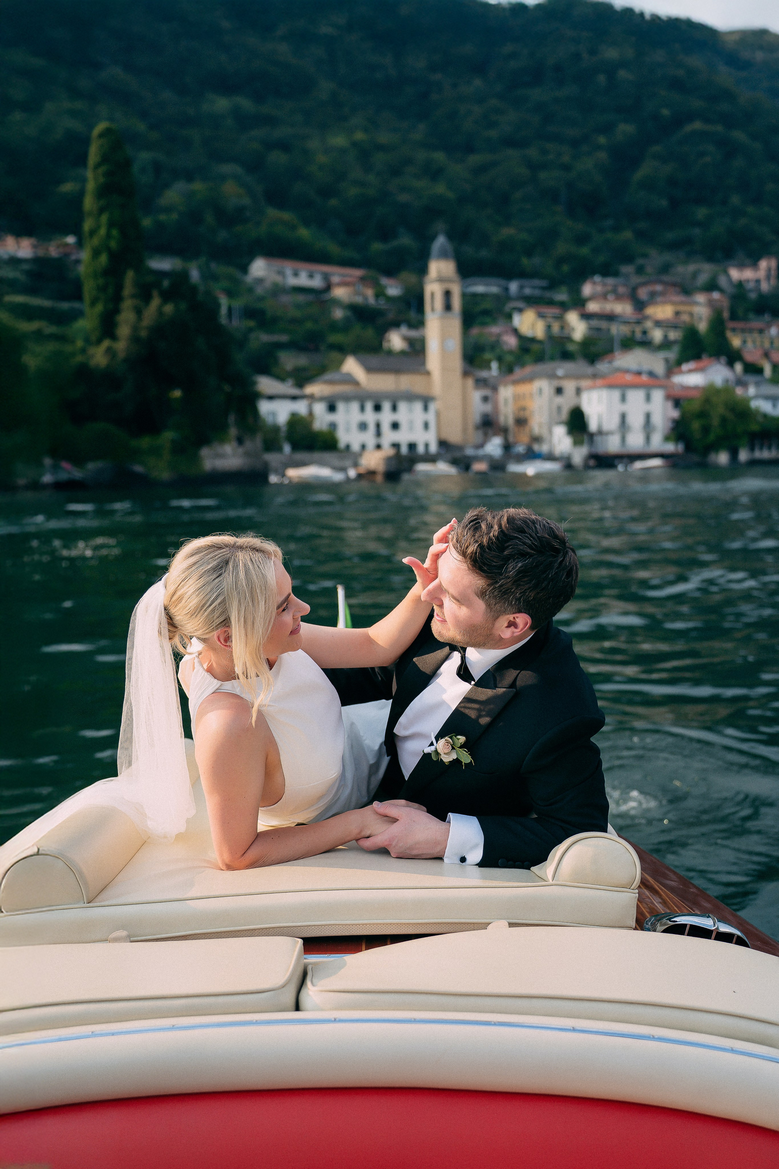 Bride and groom sitting together on the boat with the village view at Villa Lario, Lake Como, Italy