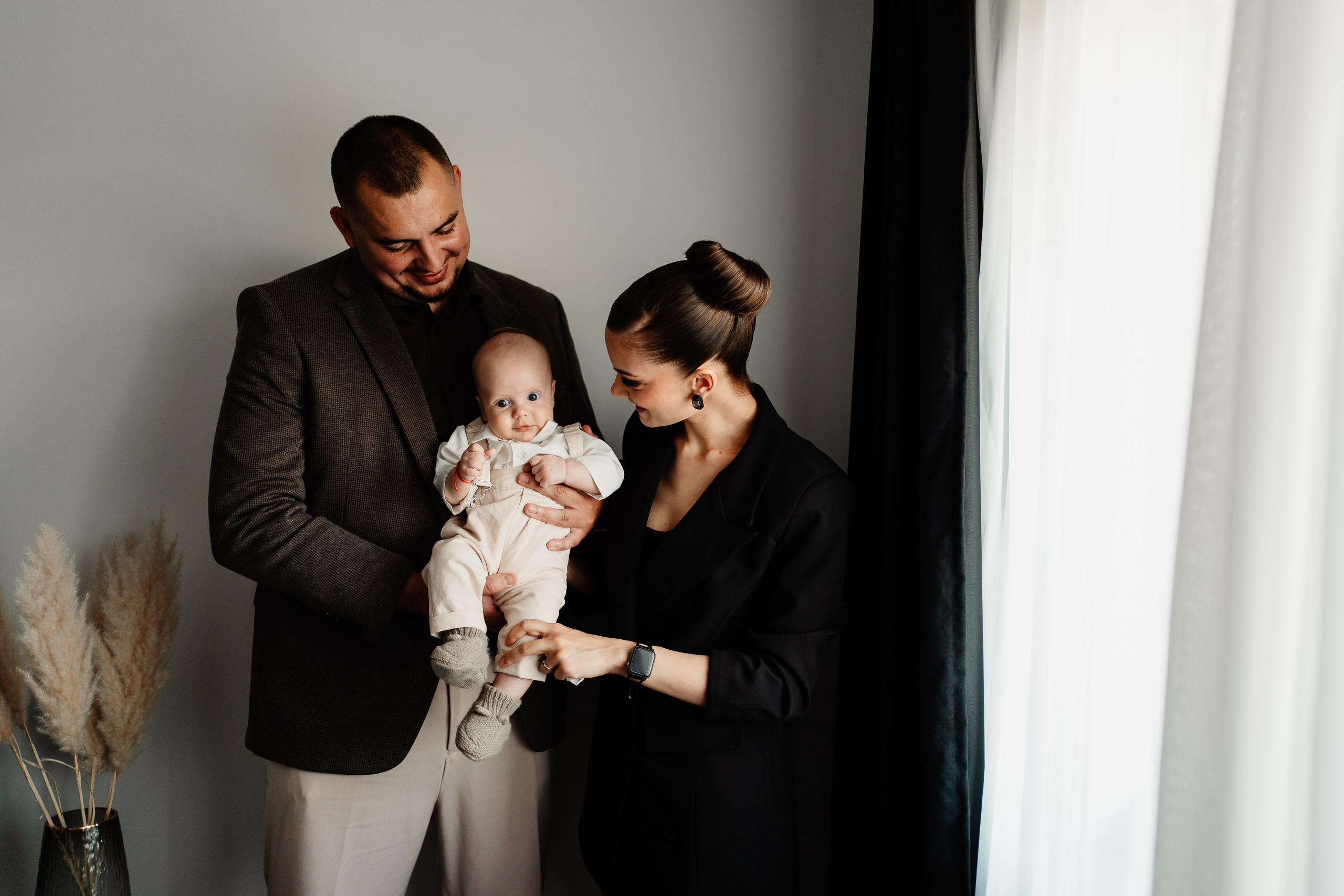 Instantaneu plin de tandrețe dintre părinți și bebeluș în ziua botezului, realizat în Craiova. Fotografie profesională de botez, capturând emoțiile autentice ale familiei într-un decor luminos și cald