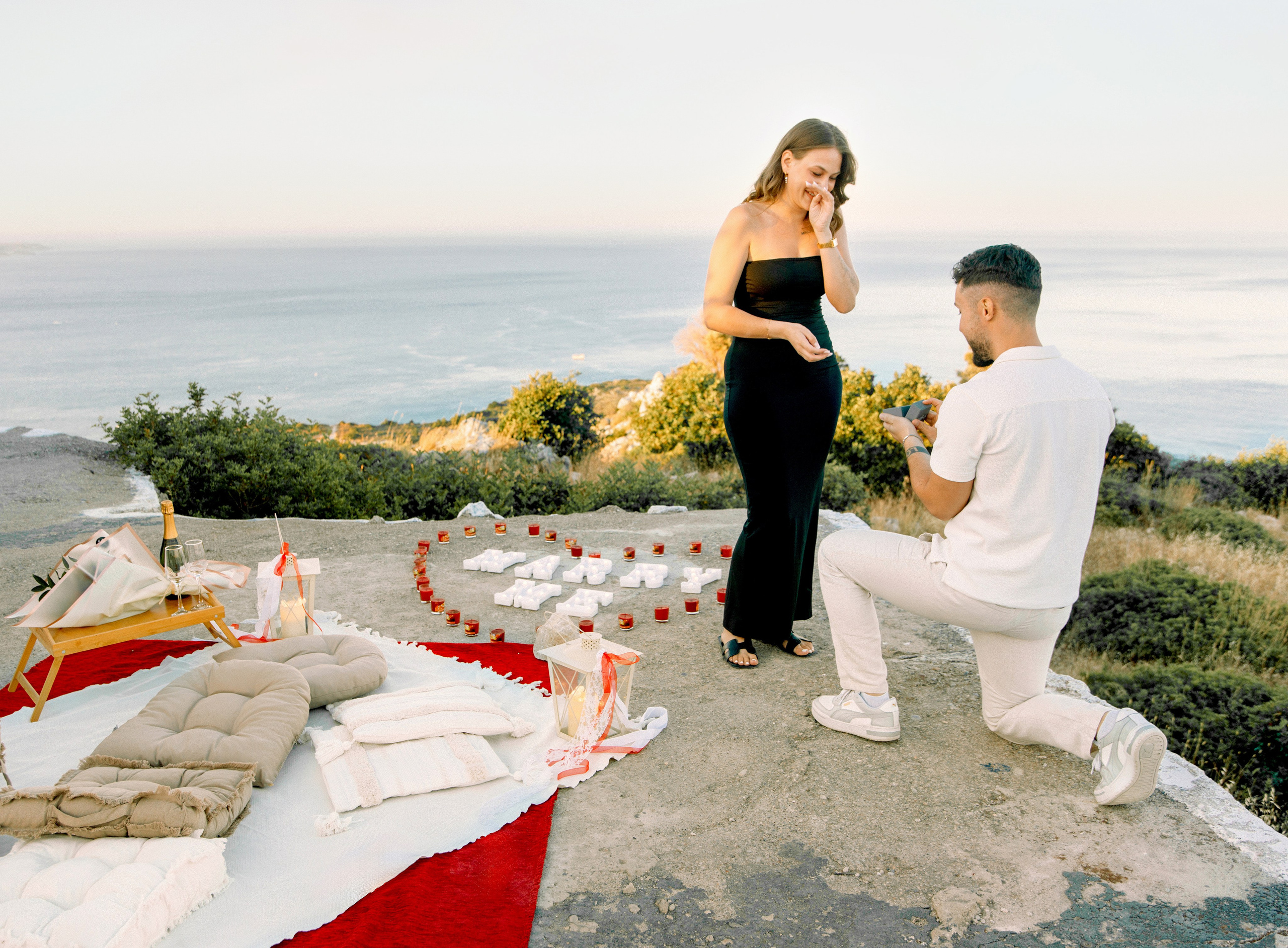 "Heiratsantrag auf dem Berggipfel: Ein Mann stellt kniend die Frage aller Fragen vor der Panorama-Kulisse von Faliraki und dem Mittelmeer."