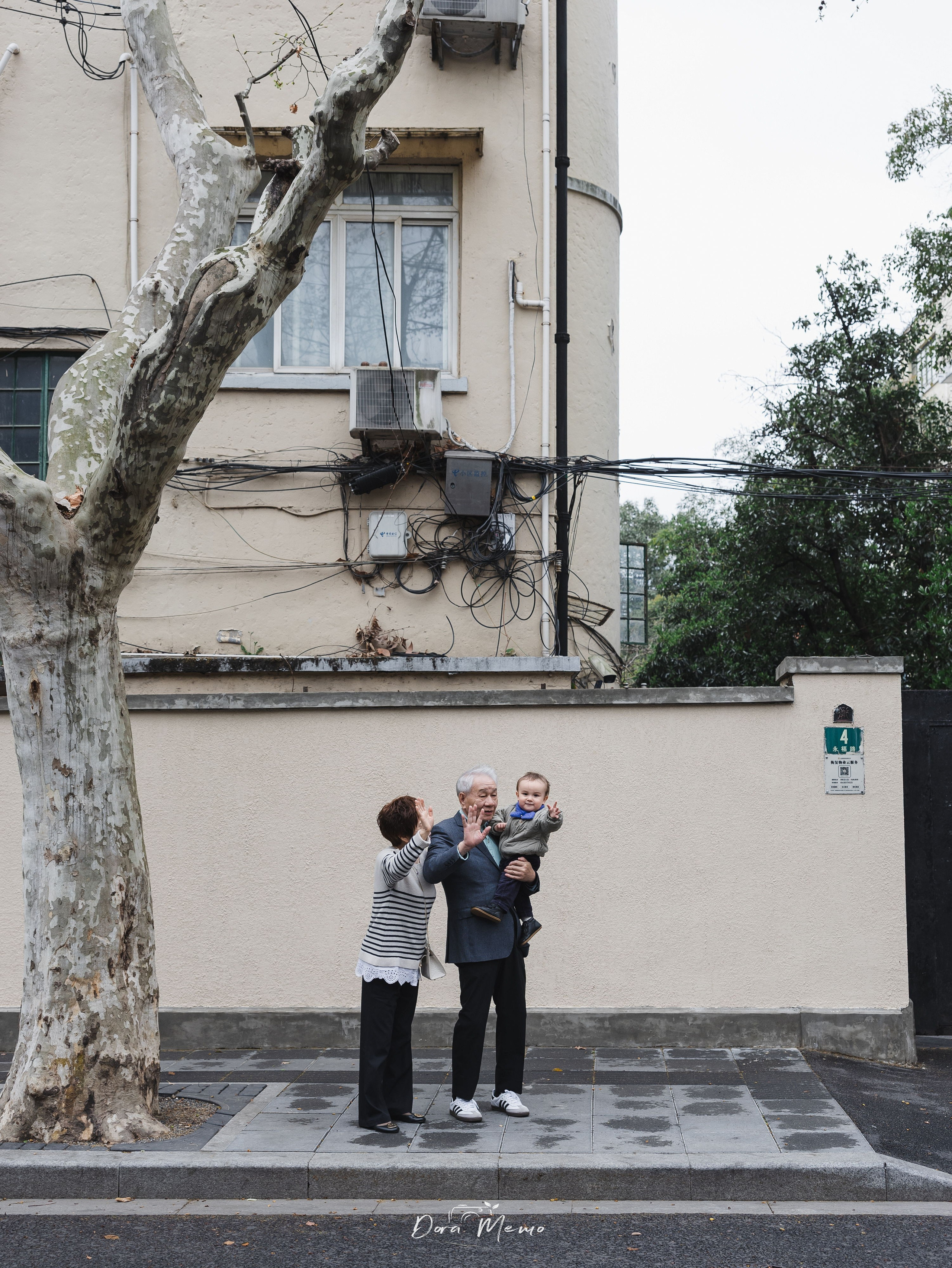 The one-year-old baby is saying "hi" to me with his grandparents across the street.