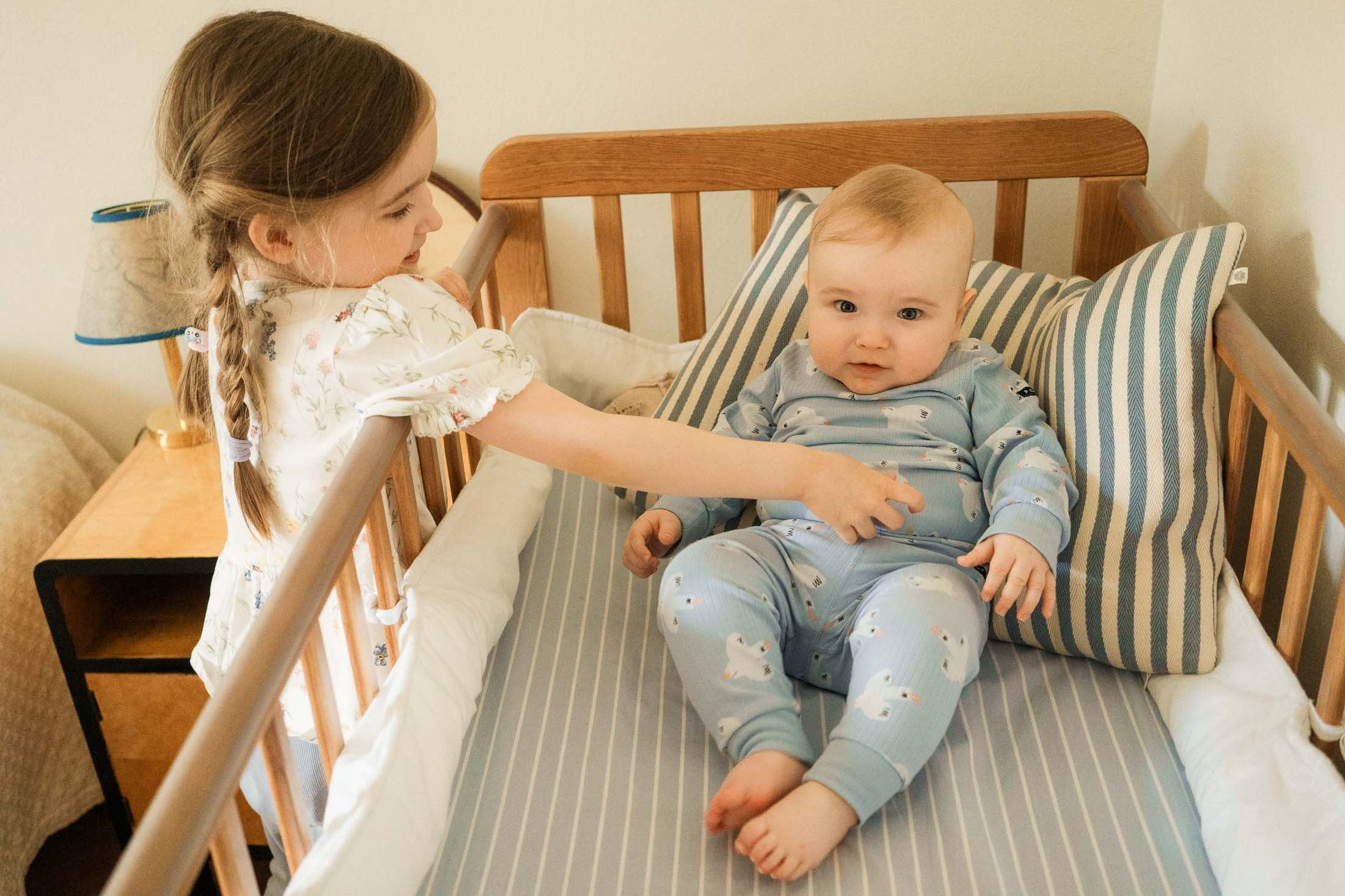 Isosisko kurkottaa pinnasänkyyn pikkuveljen luo perhekuvauksessa