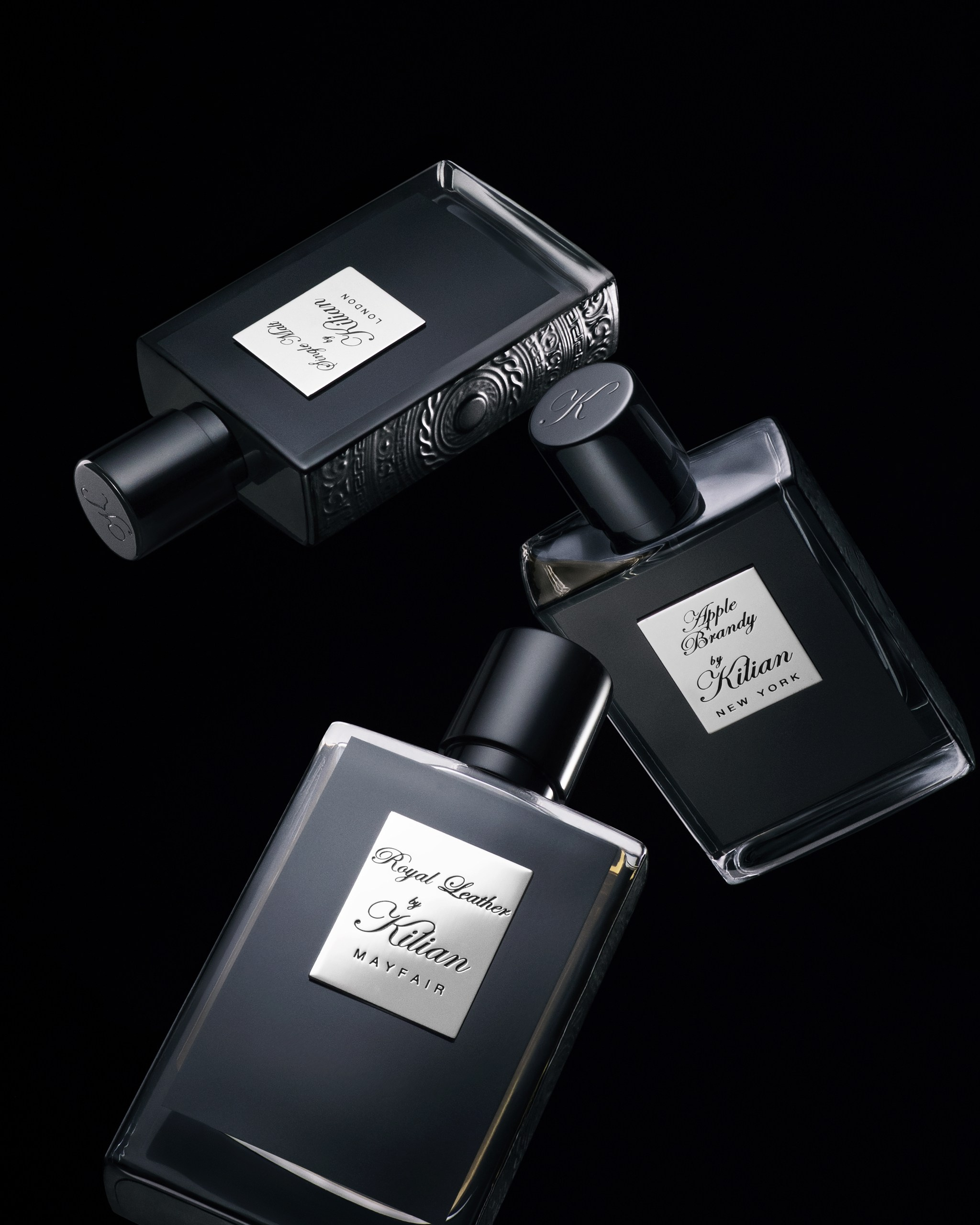 Matte black fragrance bottles on dark textured surface — high-end perfume photography.