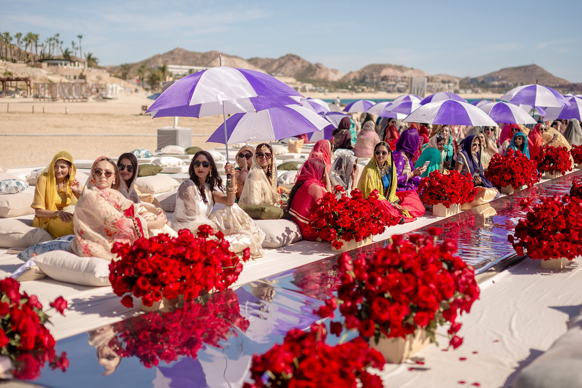 Indian wedding guests seated on cushions with umbrellas during outdoor ceremony in Los Cabos beachfront resort