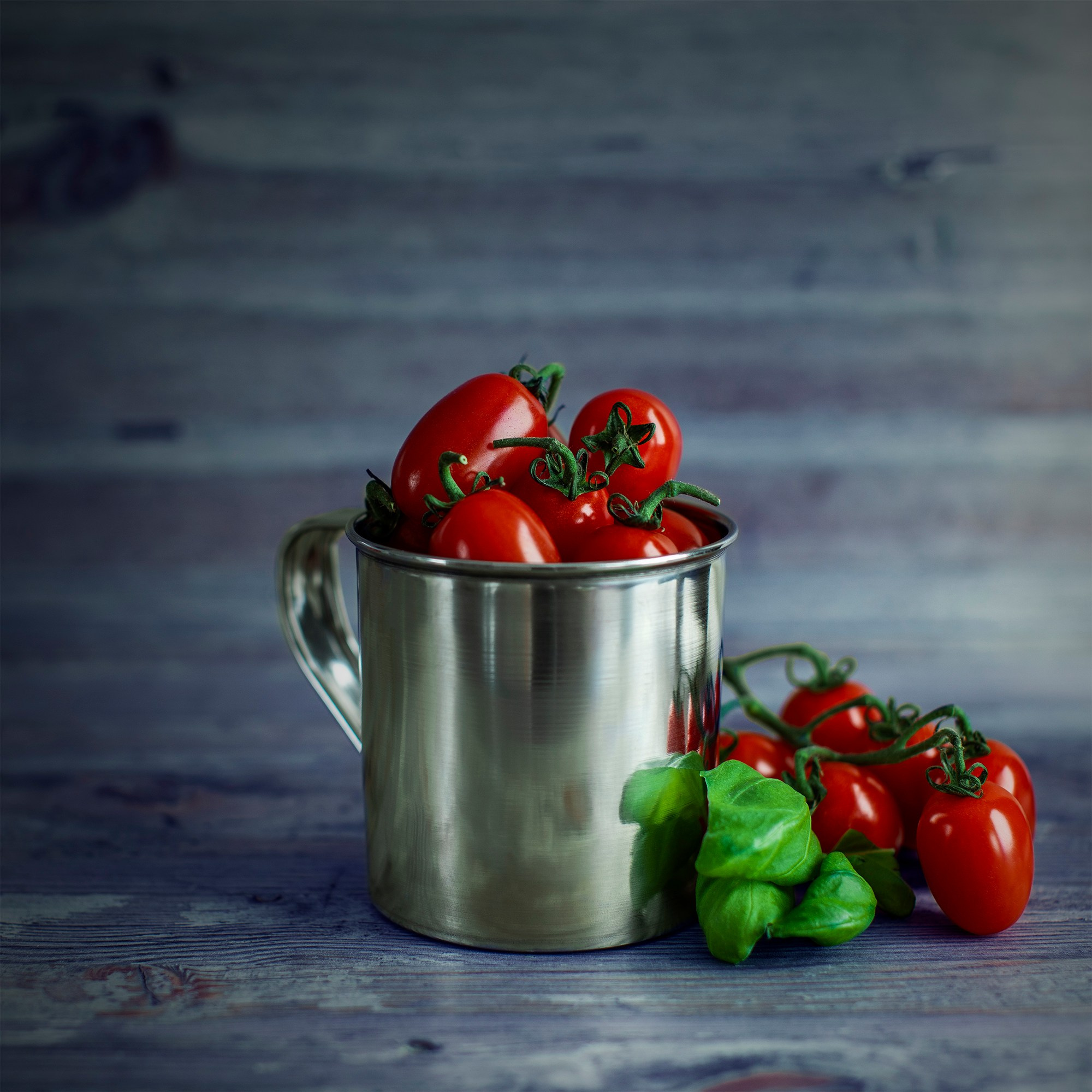 Photographer Roman Djuzev - Cherry tomatoes in a metal mug with basel leaves on a wooden table.