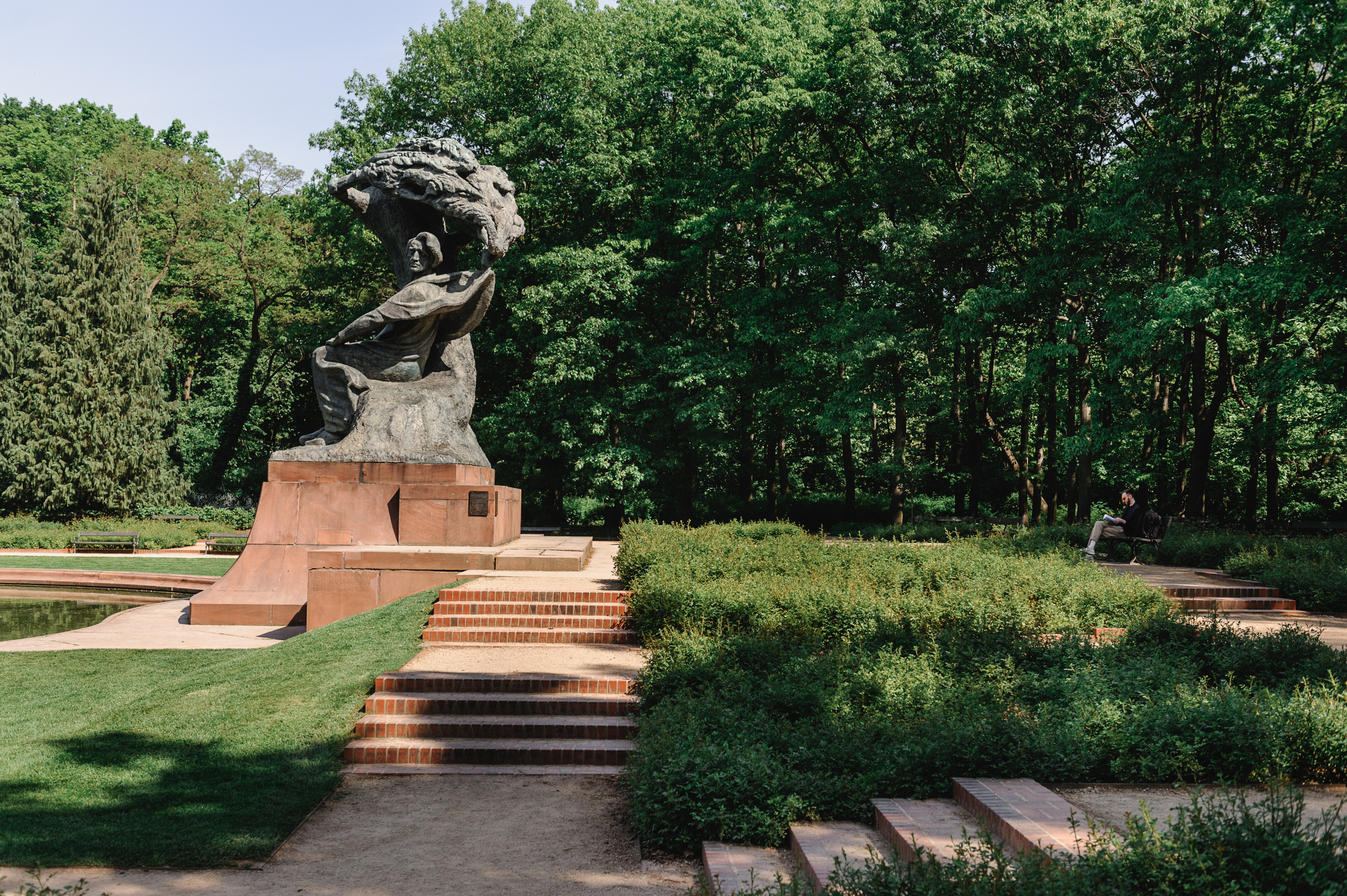 The Chopin monument in Lazienki Park and Dmitry Solodkiy sitting on a bench, reading a book.