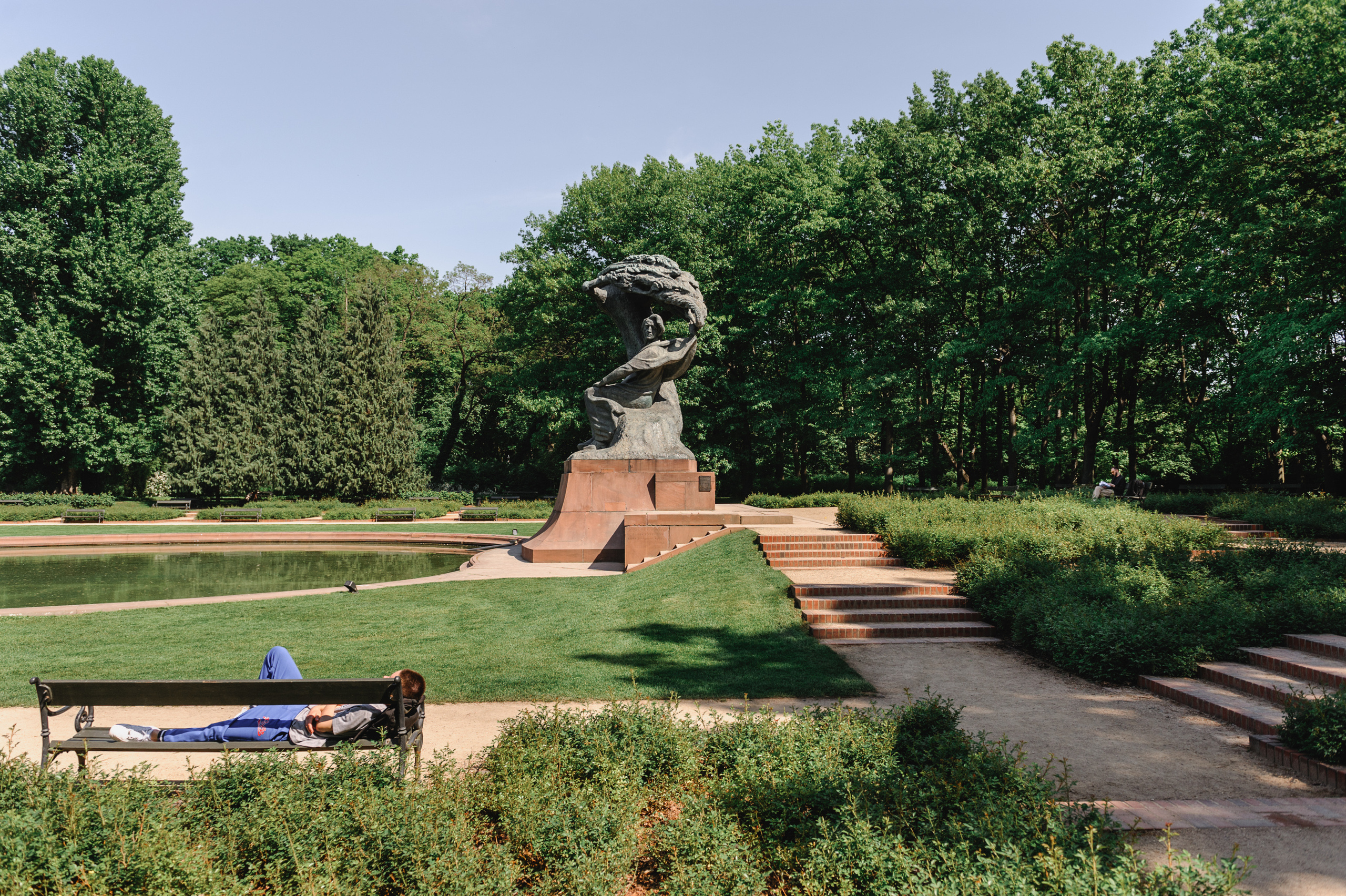 The Chopin monument in Lazienki Park and a sleeping person on a bench.