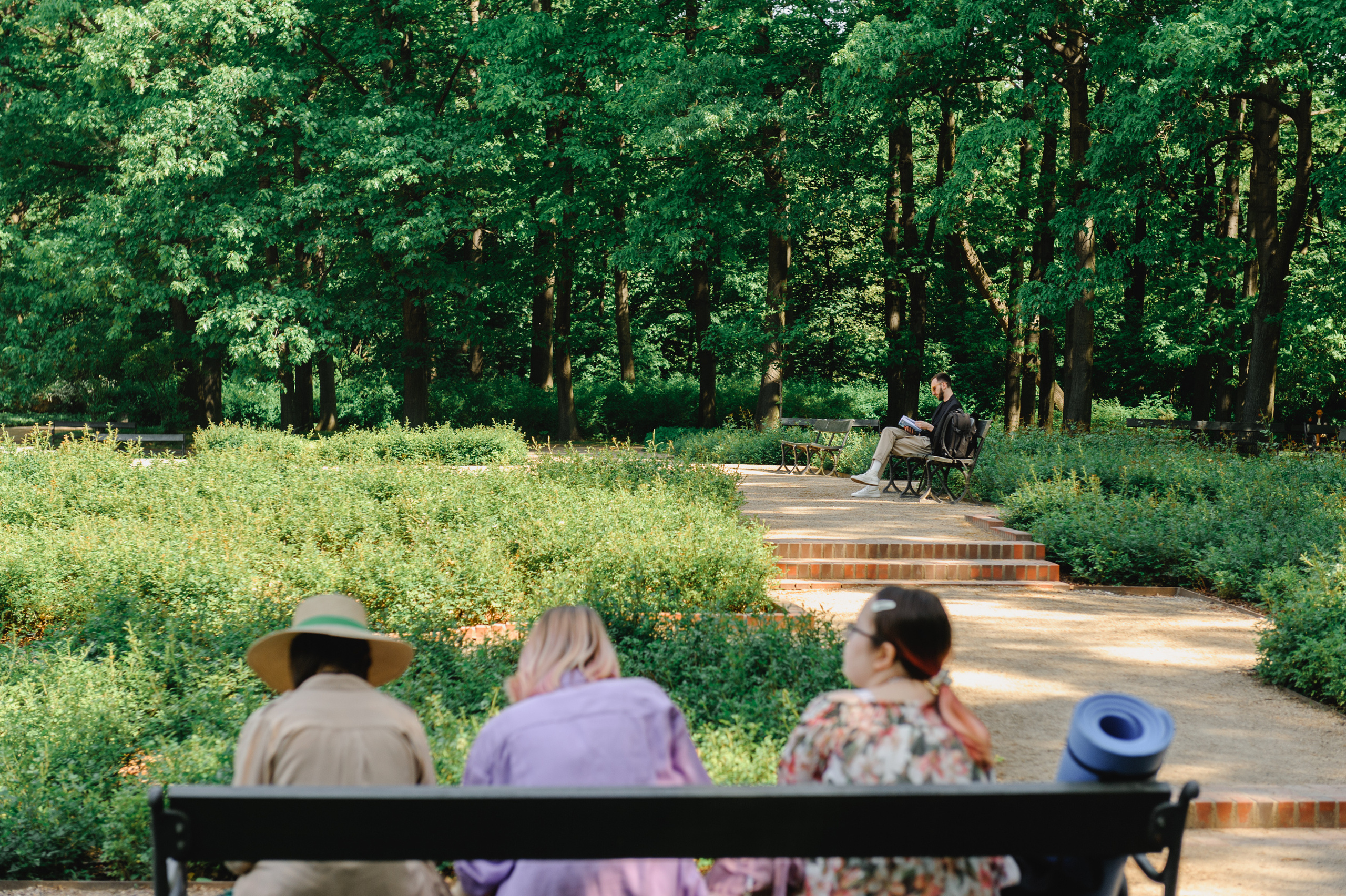 Four people sitting back to back on a bench. Dmitry Solodkiy is reading a book in the distance.