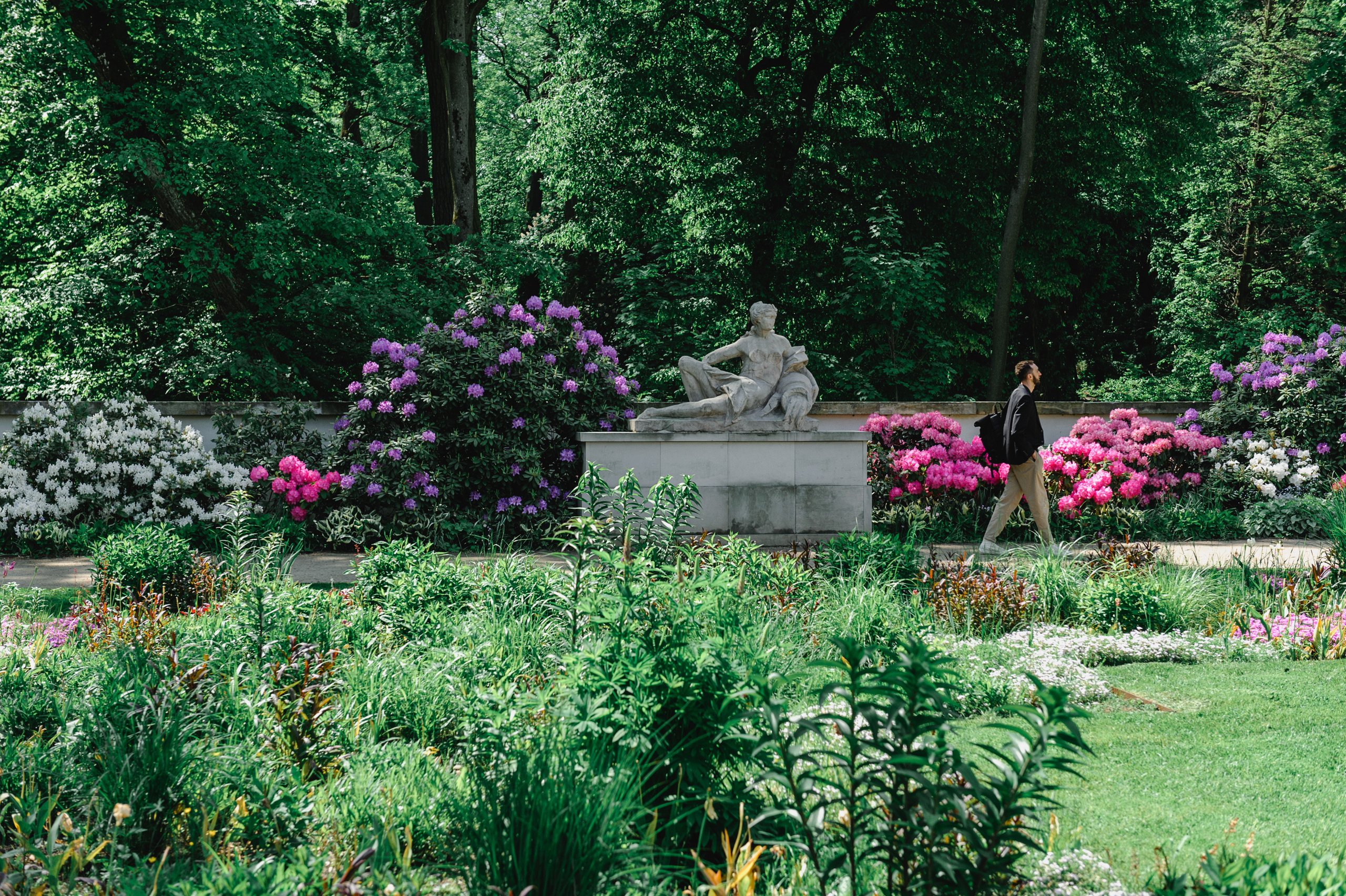 Dmitry Solodkiy strolls through Lazienki Park. A sculpture and flower beds in the background.