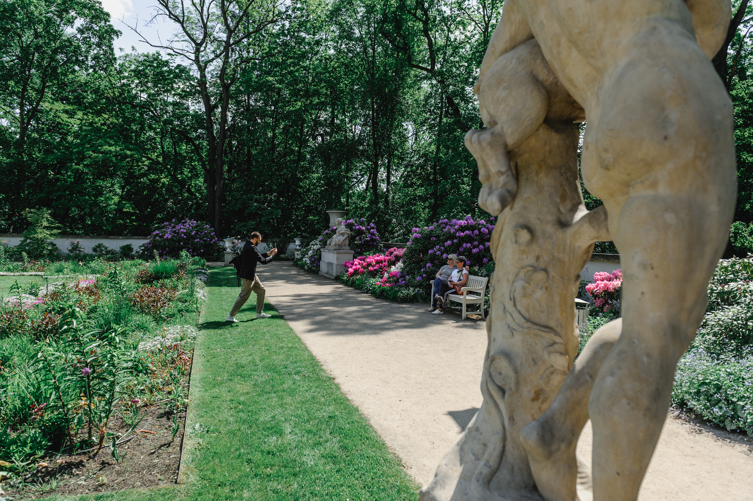 Dmitry Solodkiy photographs charming ladies in Lazienki Park in Warsaw. The buttocks of a standing sculpture in the foreground.