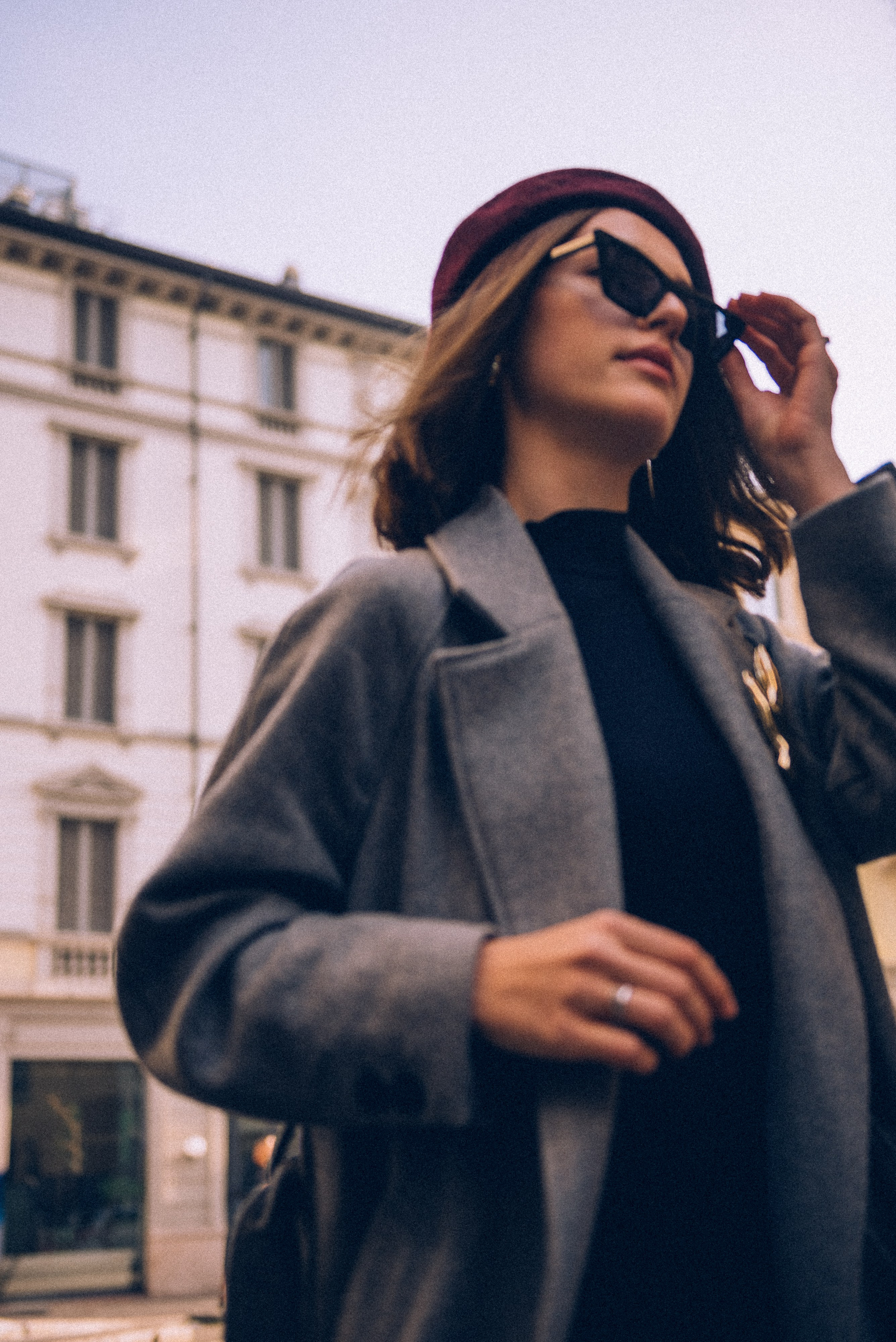 Close-up portrait of a fashionable woman in Milan wearing a burgundy beret and statement sunglasses, captured in soft morning light