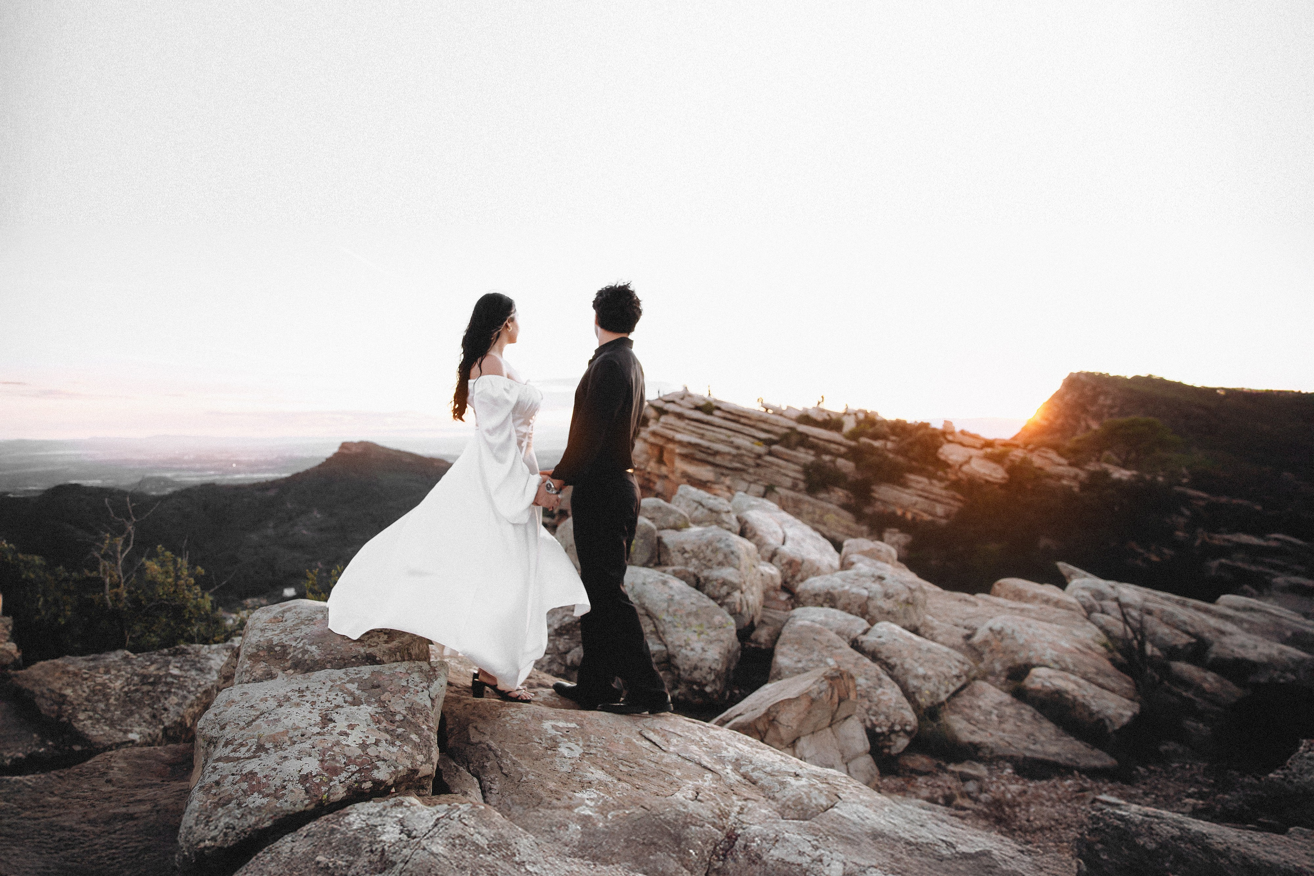 Bride sitting beside the groom on natural stone formations during a secluded destination elopement in Barcelona, Spain. The dramatic landscape enhances the cinematic and intimate feel of this mountain wedding session.