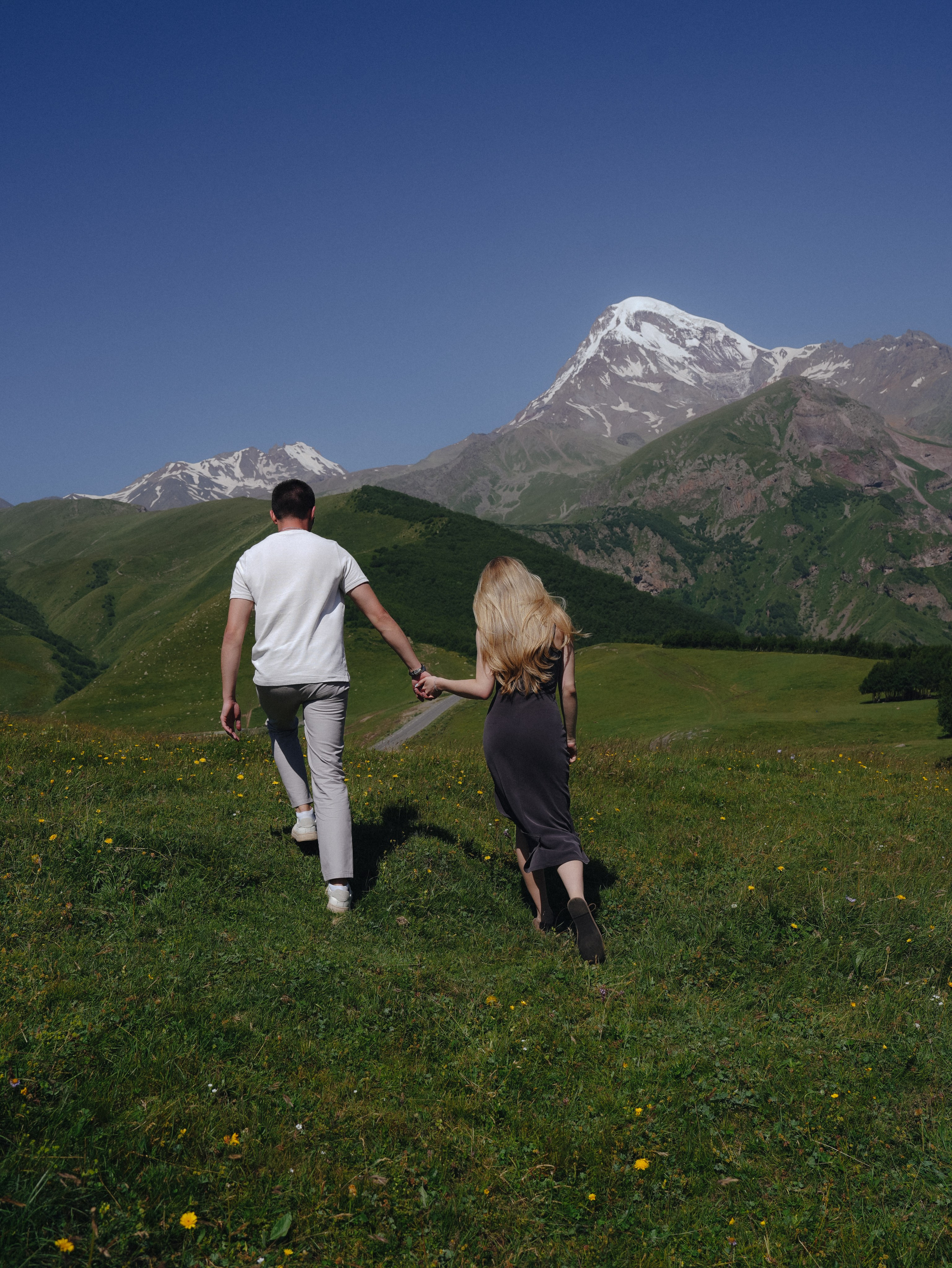 Couple walking through mountain meadow after summer proposal in Kazbegi Georgia