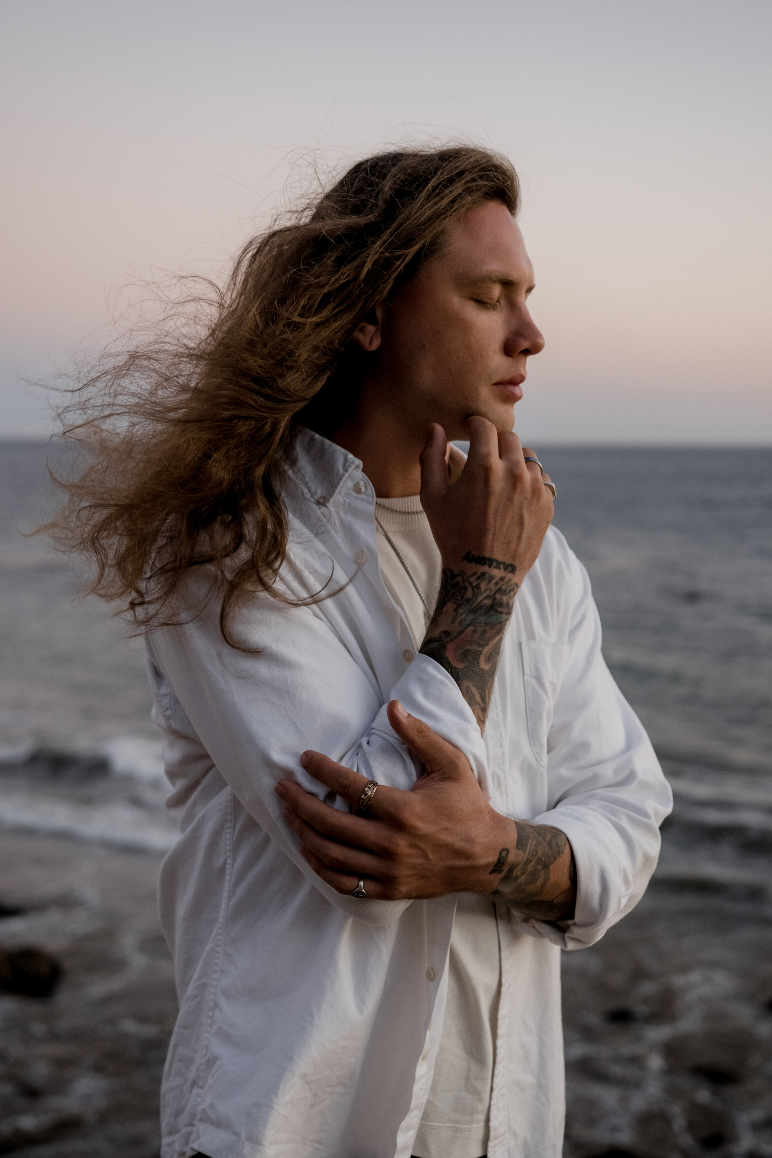 Portrait of a model standing against the ocean backdrop during sunset, showcasing minimalist beach fashion.