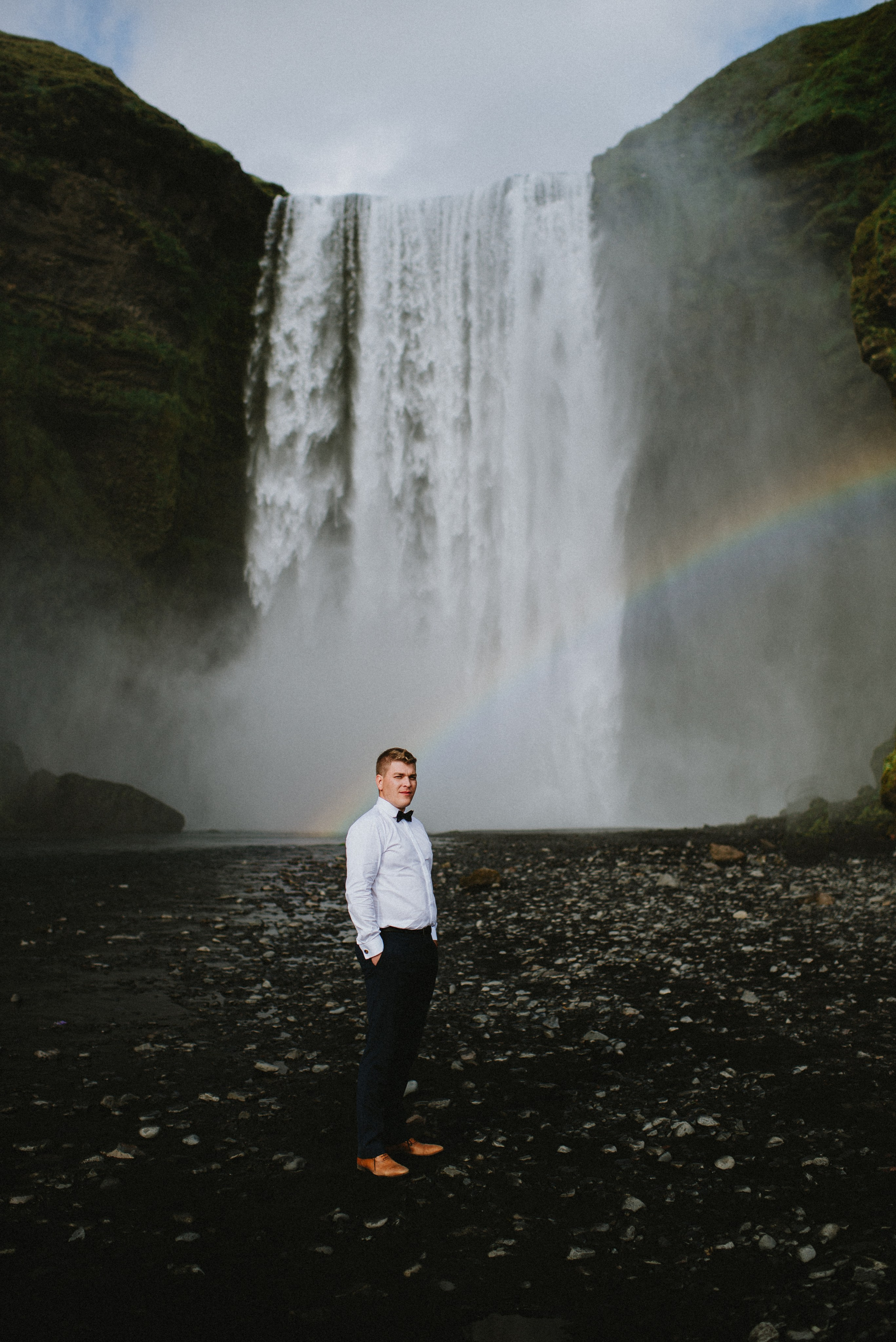 Groom lifting the bride in the air in front of the roaring Skógafoss waterfall.