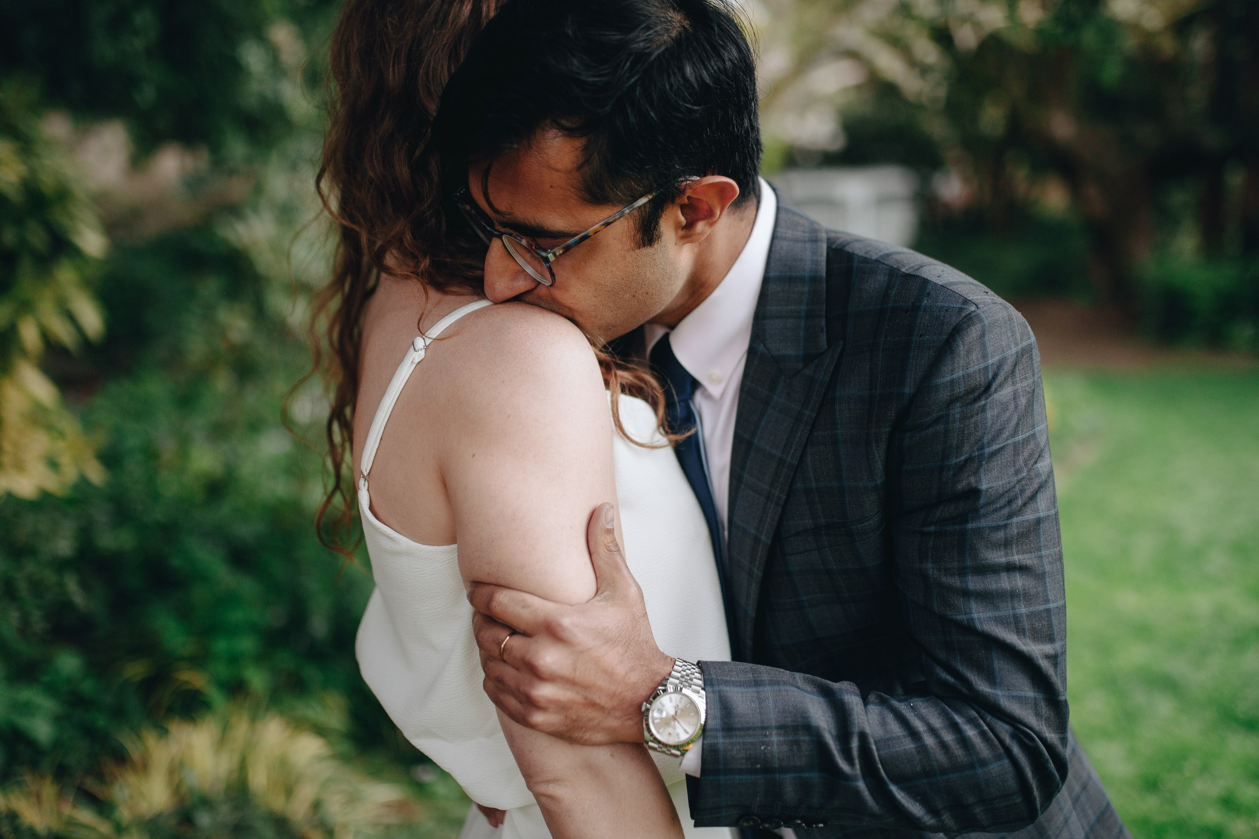 Bride kissing groom’s forehead in garden, intimate moment