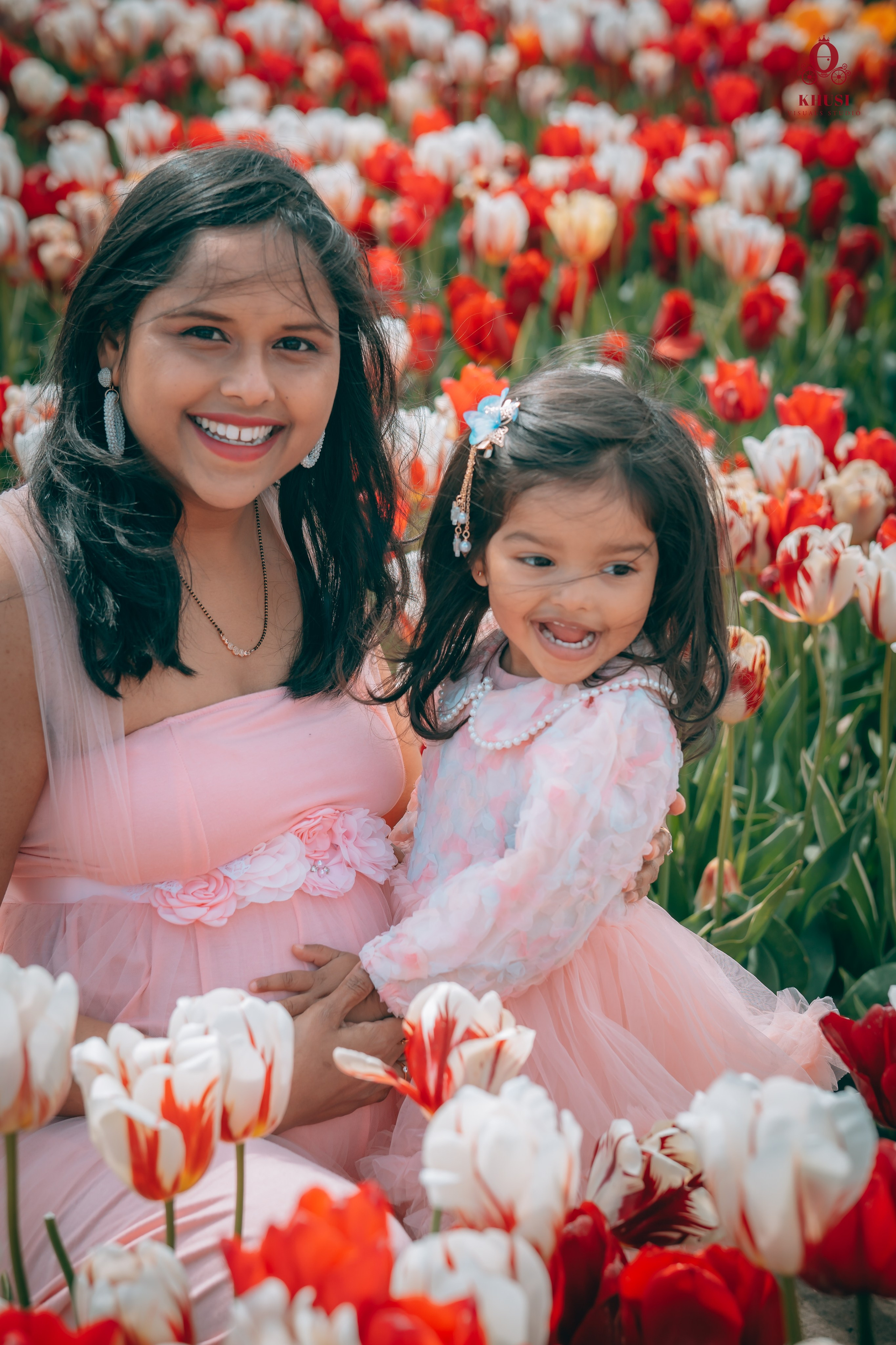 A pregnant woman holding her daughter in a white and red tulip fields in netherlands