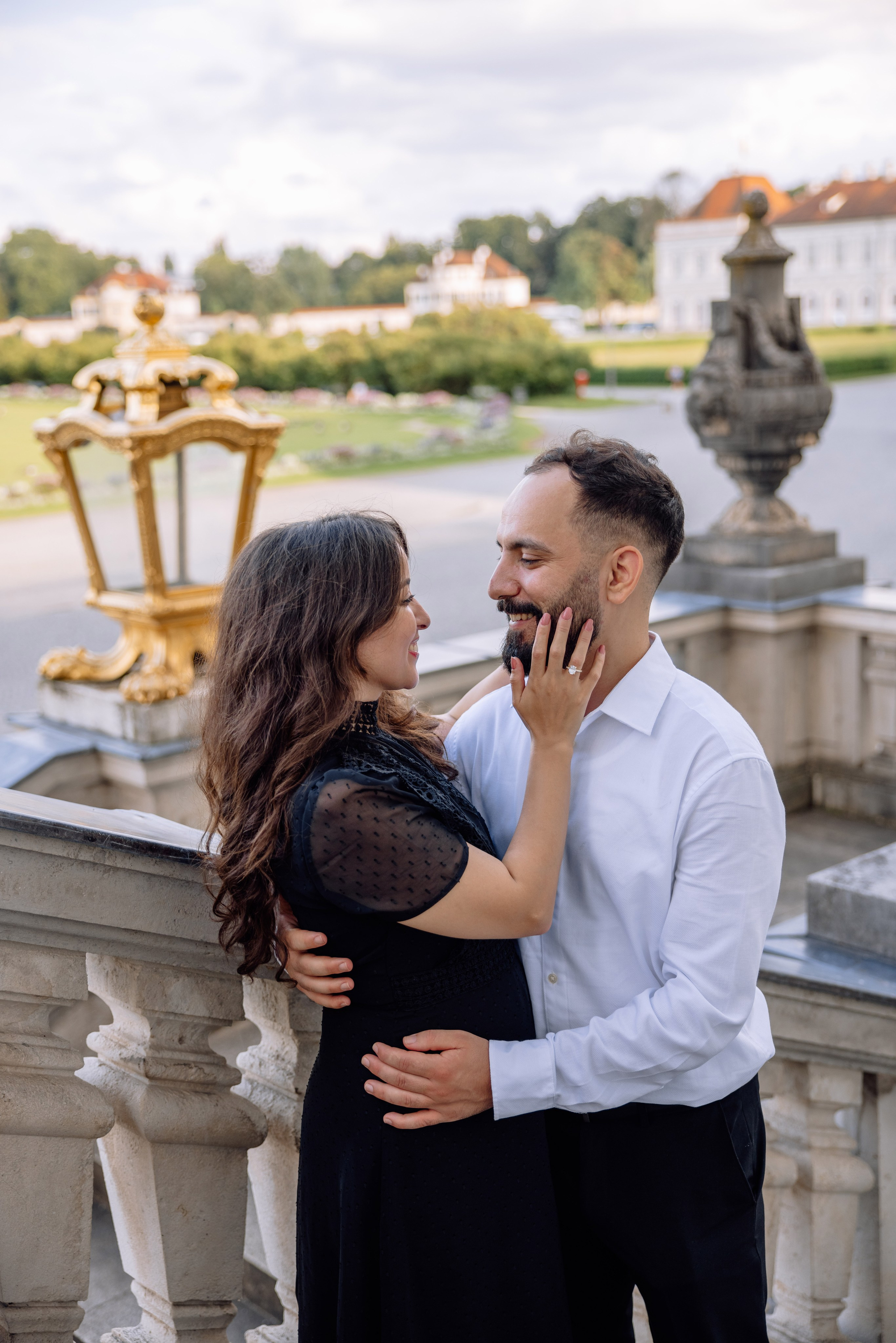 Braut streichelt das Gesicht des Bräutigams vor dem Schloss Nymphenburg