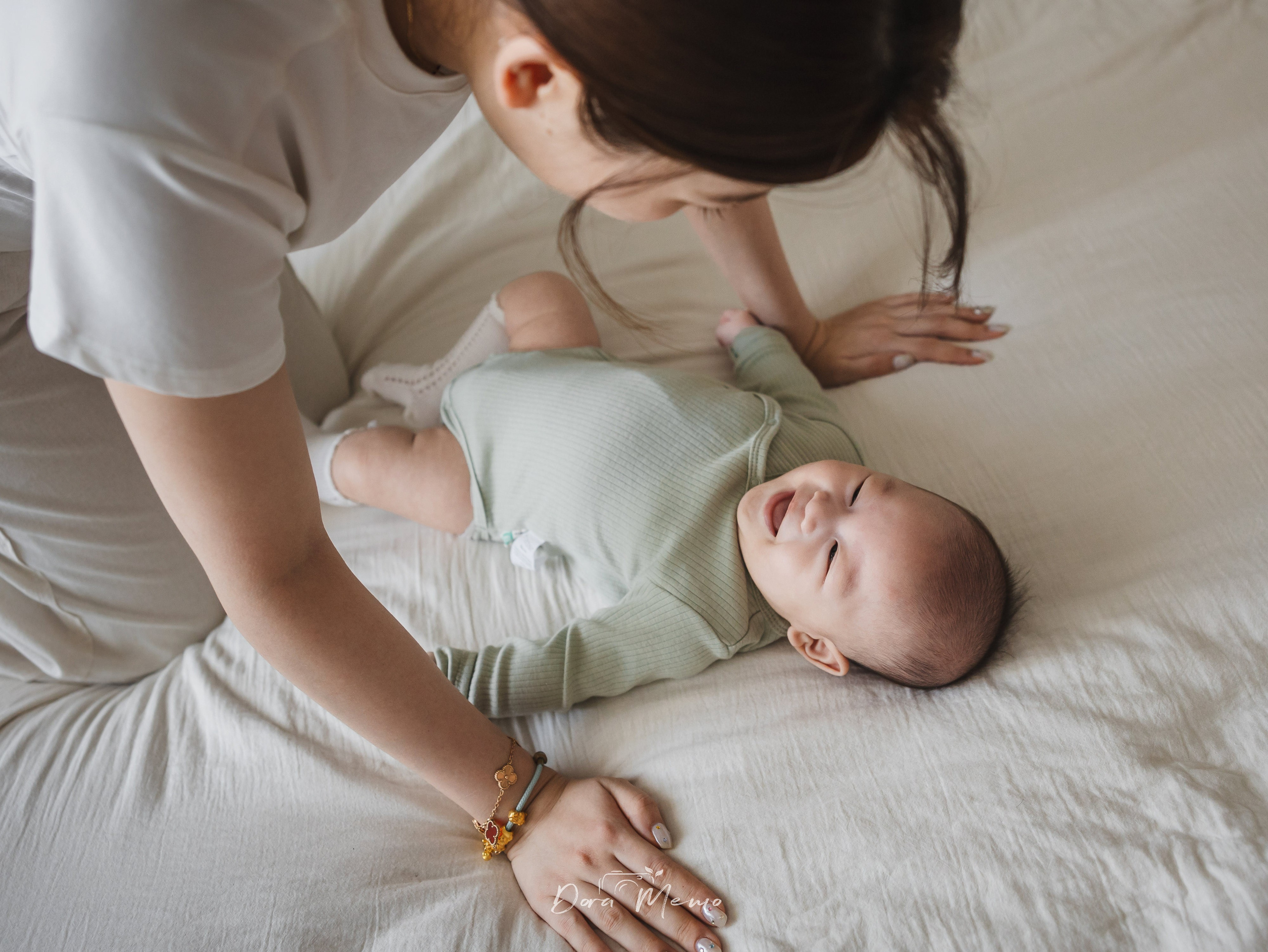 A baby bursts into laughter while playing with mom on the bed