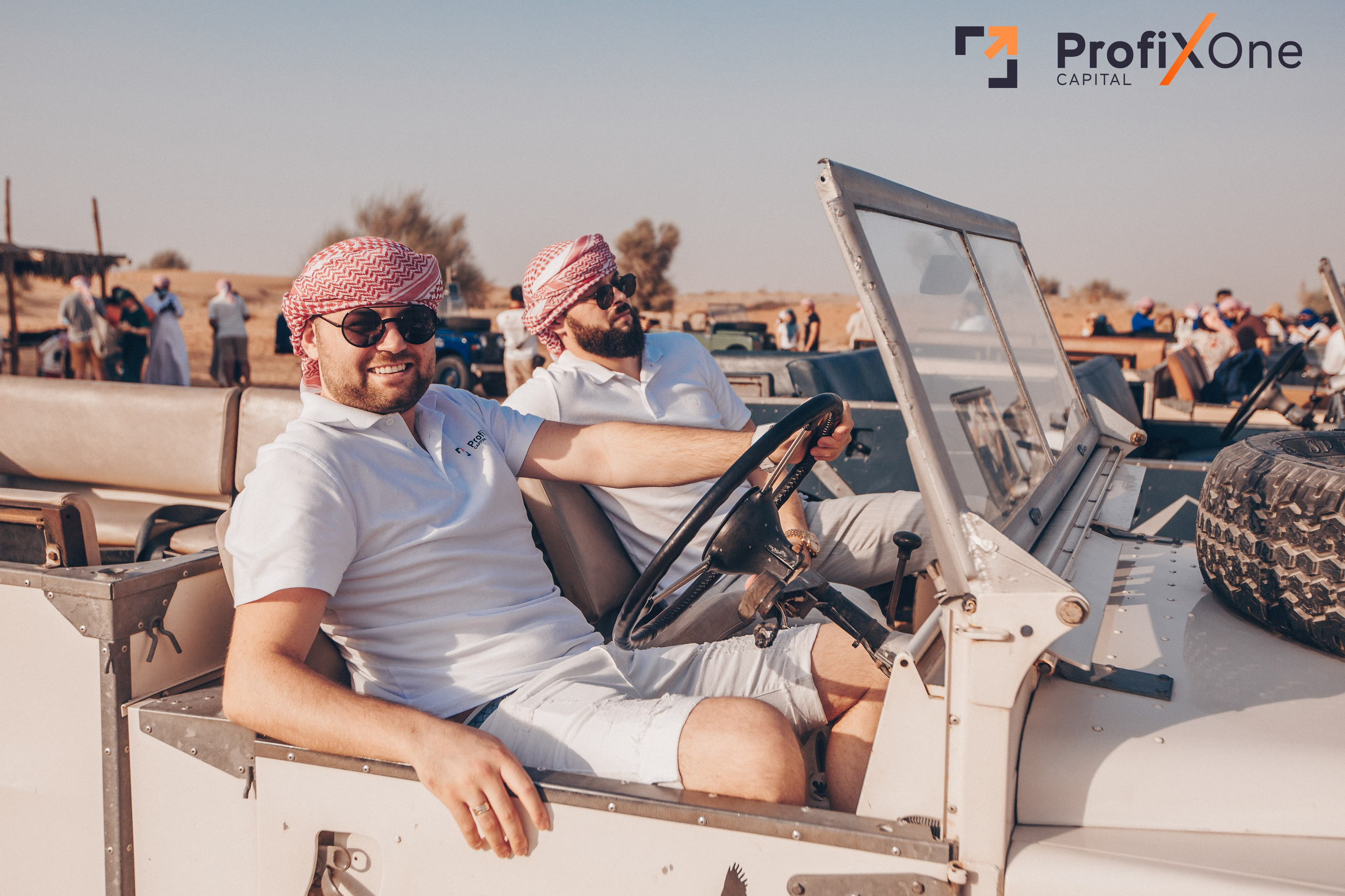 Two men are sitting in a retro range Rover. Against the background of a sandy Duvai sunset