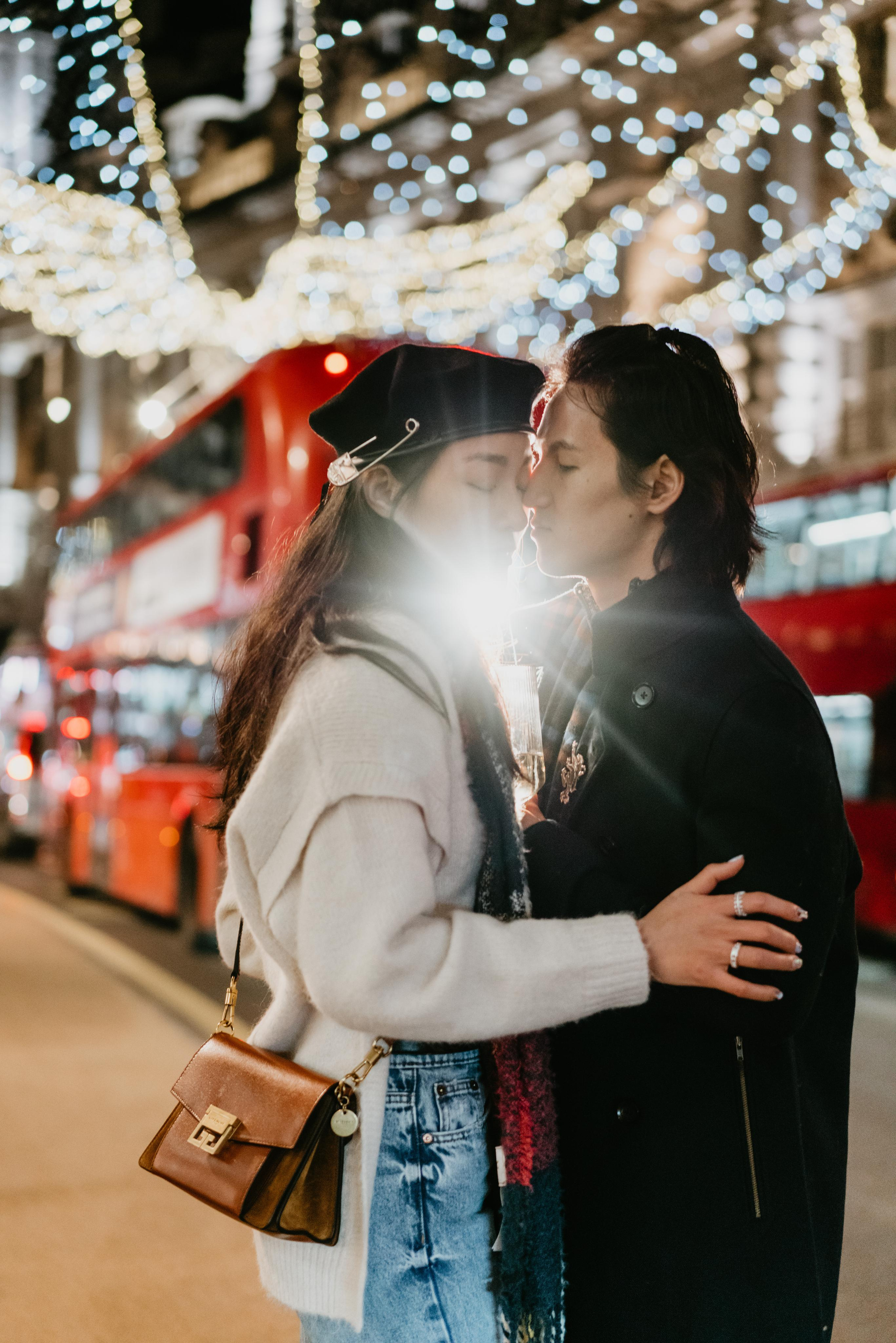 couple kissing on the street with Christmas lights 