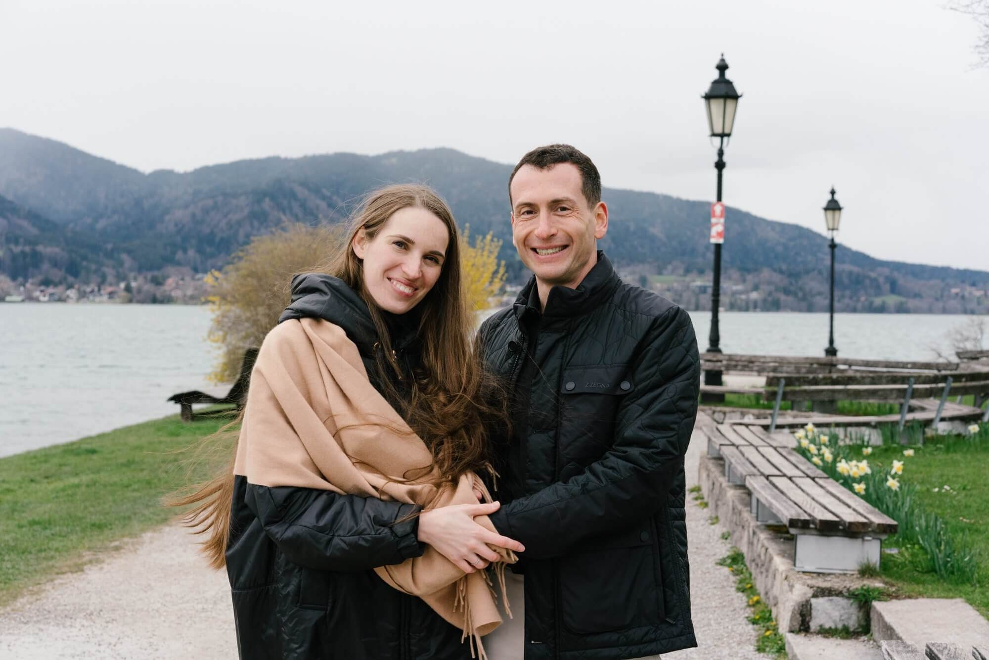 Couple sitting on a bench at Tegernsee lake promenade with blooming yellow tree and lamp post Bavaria Germany