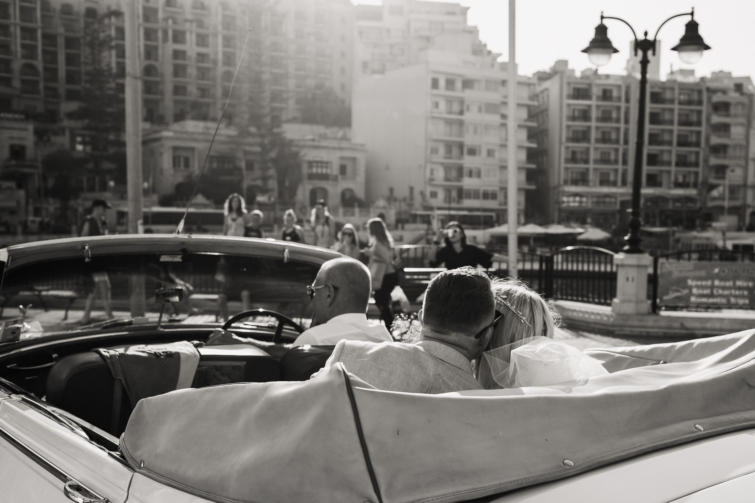 Bride and groom kissing in the vintage car are about to leave 