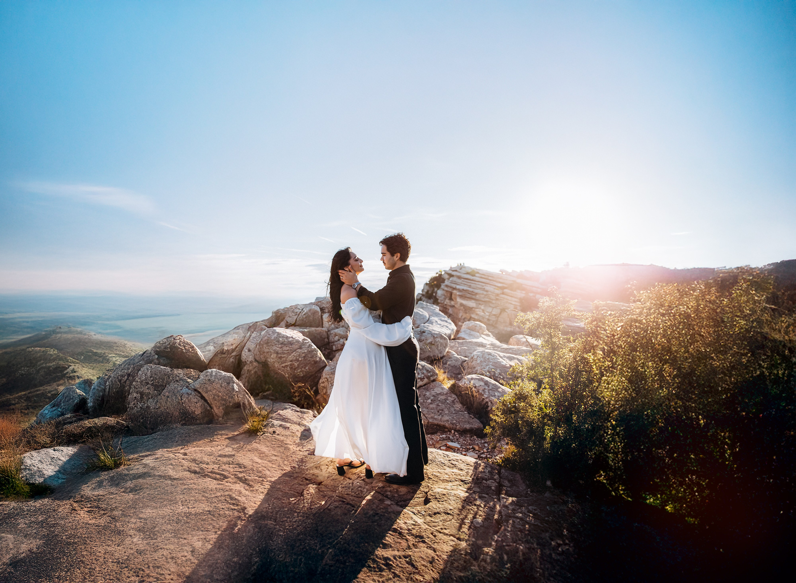 Bride and groom embracing on a mountain cliff at sunset during an intimate destination wedding in Barcelona, Spain. The golden light and rocky landscape create a romantic elopement atmosphere with panoramic views.
