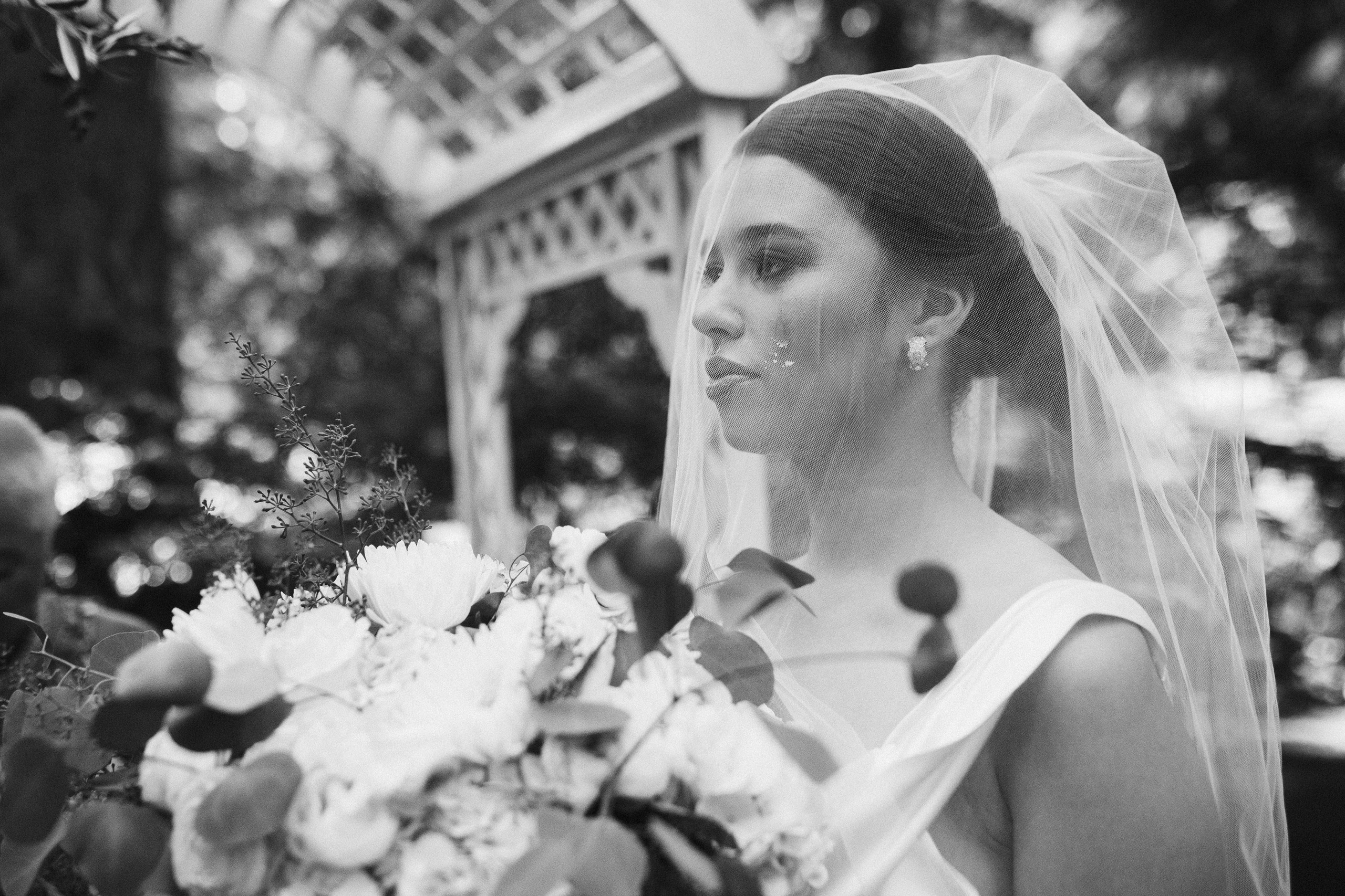 Bride under veil holding bouquet, black and white photo