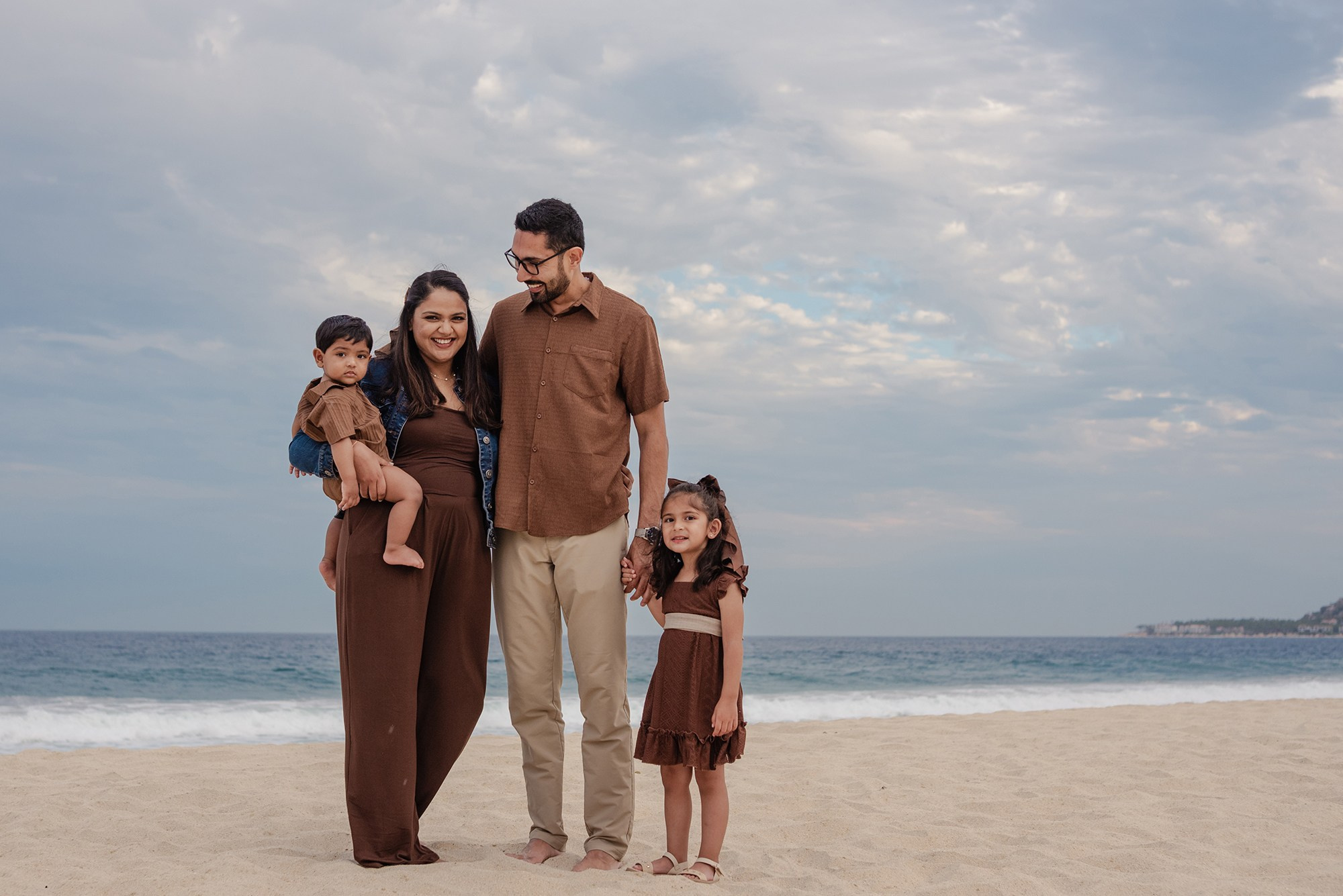 Family of four standing together on the beach at Hyatt Ziva Los Cabos, dad holding his toddler son