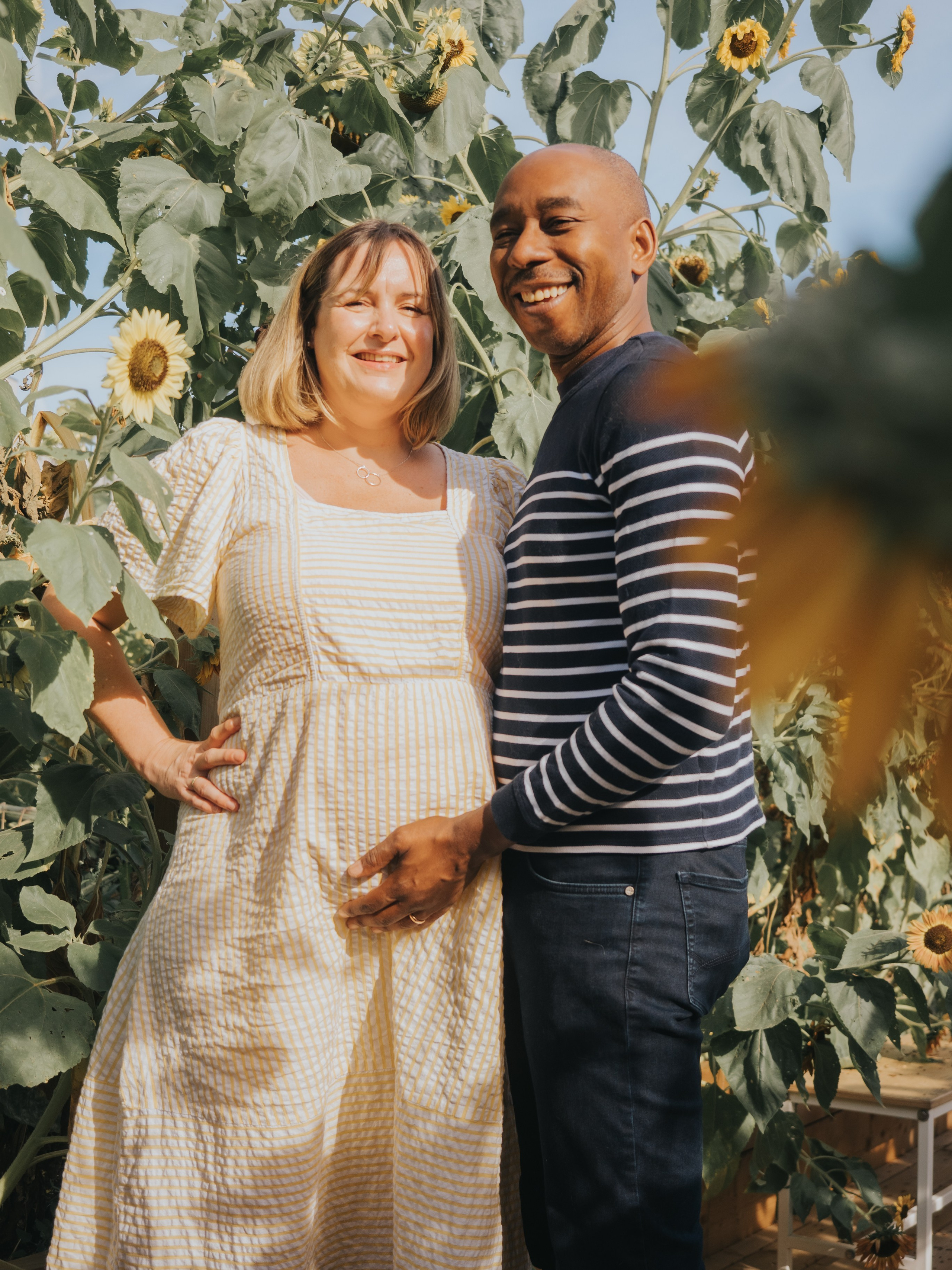 A couple with a pregnant woman surrounded by sunflowers.